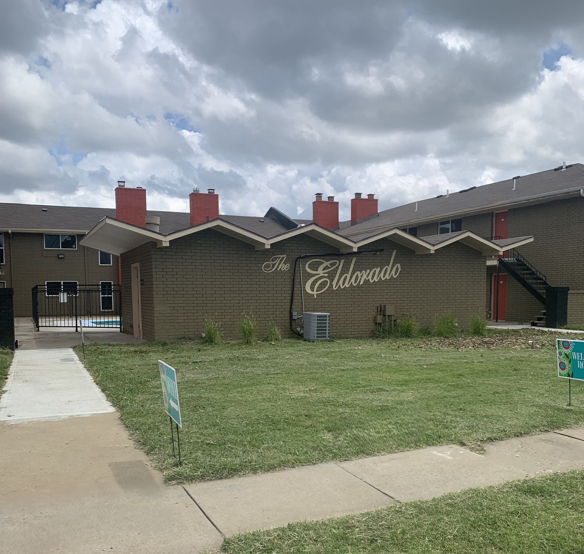 "The Eldorado" apartment complex exterior on a cloudy day, featuring brown brick buildings and green lawn.