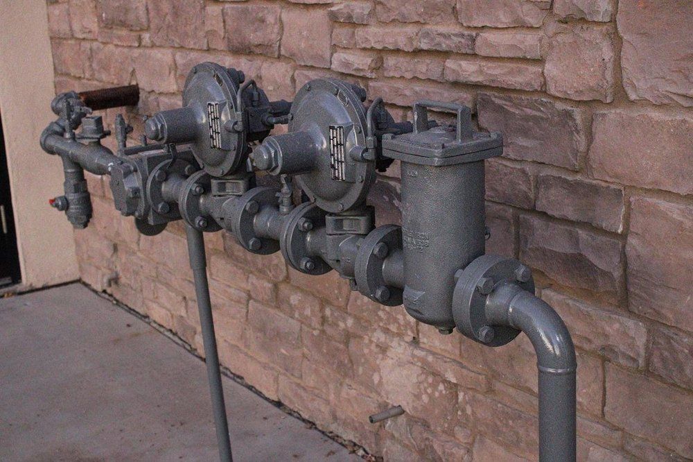 Gas regulator system on a brick building exterior, painted gray.
