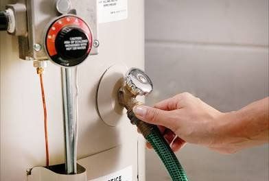 Person draining a hot water heater with a hose, steam visible.