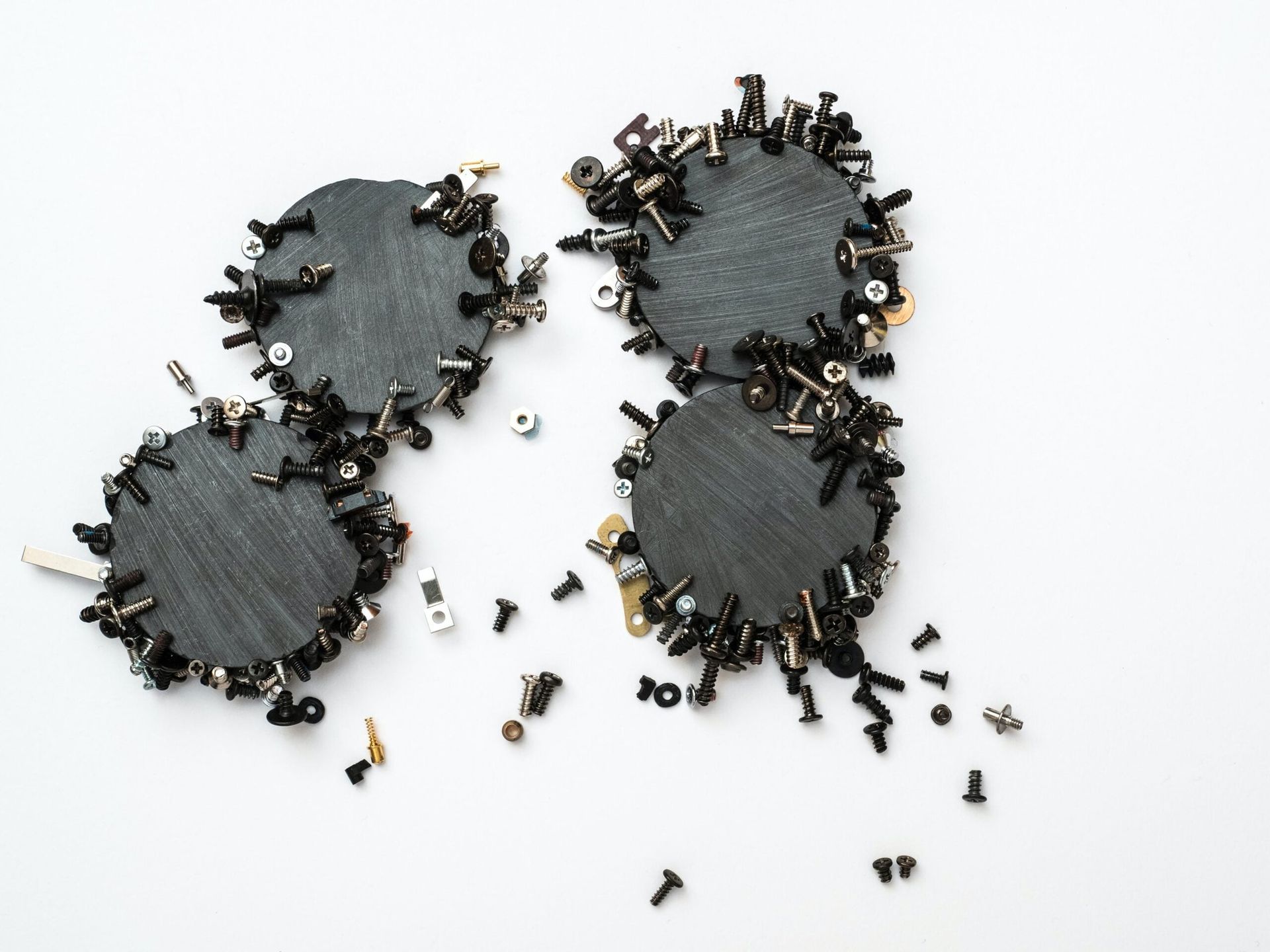 Four black, circular shapes surrounded by small screws, nuts, and bolts on a white surface.