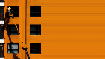A worker in a lift, servicing windows on a bright orange building.