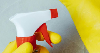Hand in yellow glove holding red and white spray bottle.