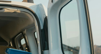 White van's open door showing the interior, blue container, and the outside landscape.
