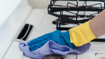 A person wearing a yellow and blue glove is cleaning a white stovetop with a blue cloth.