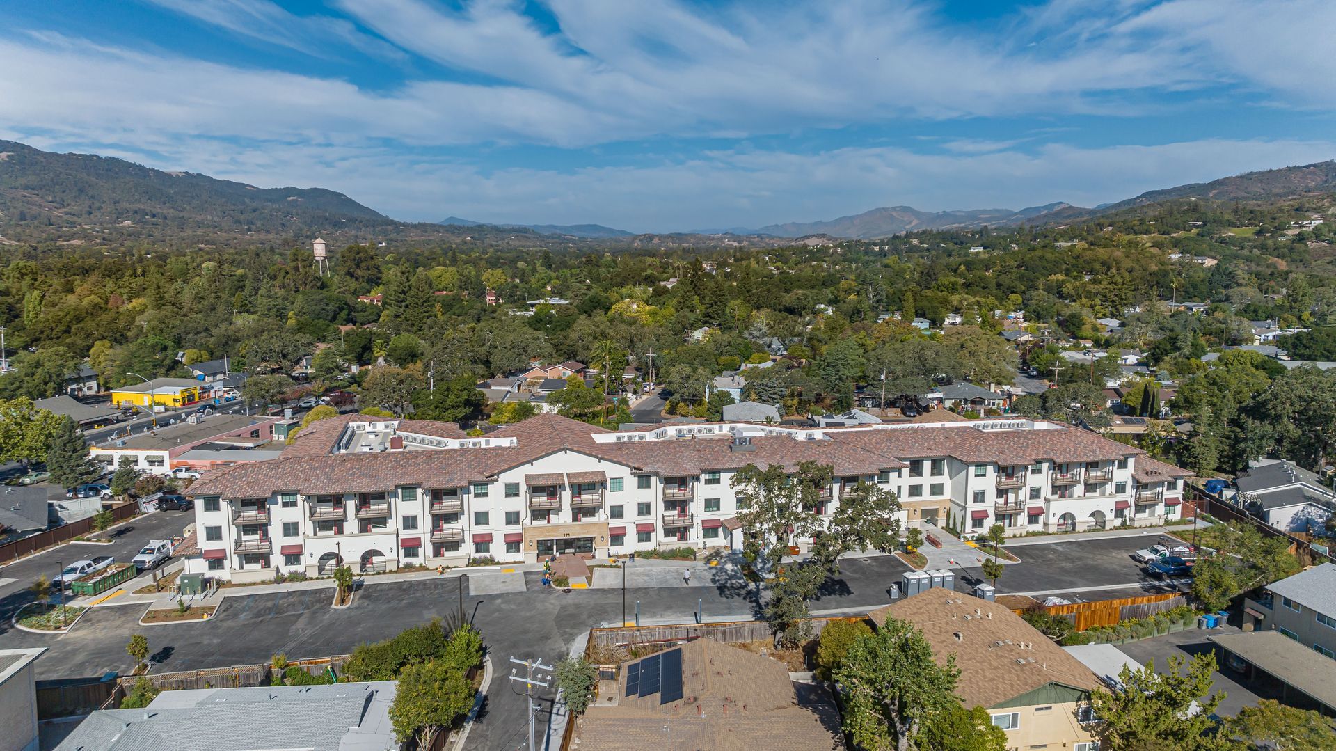 Aerial view of a white apartment complex amid trees and hills under a blue sky