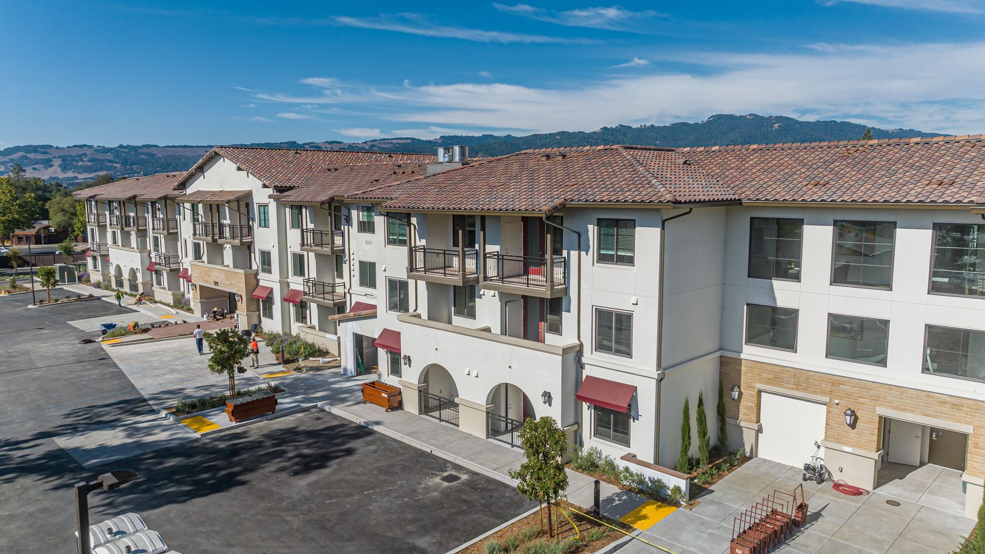 Apartment complex with red-tiled roofs and balconies beside a parking lot under a clear blue sky