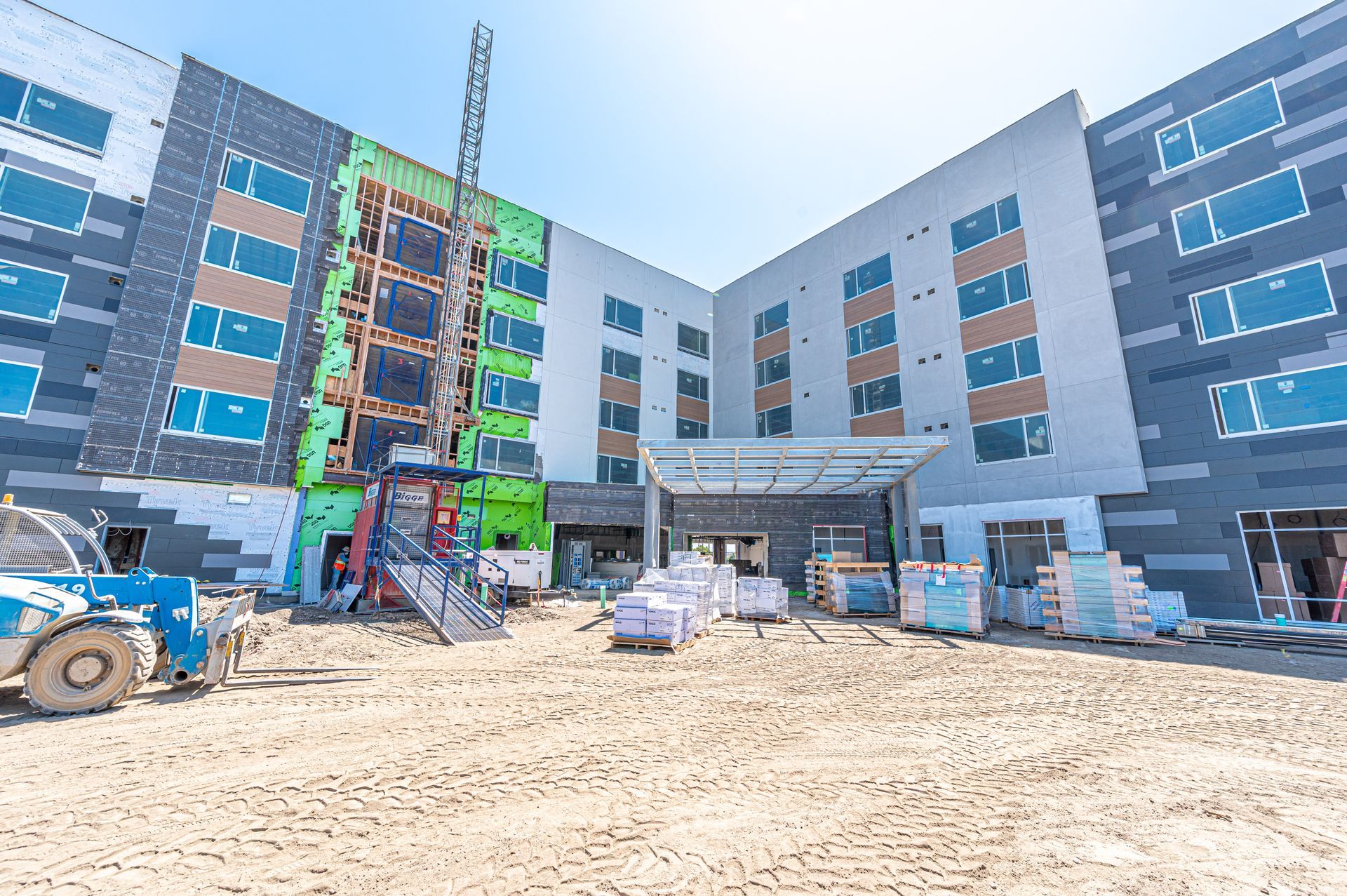 Construction site outside a modern apartment building with scaffolding, blue windows, and workers’ equipment
