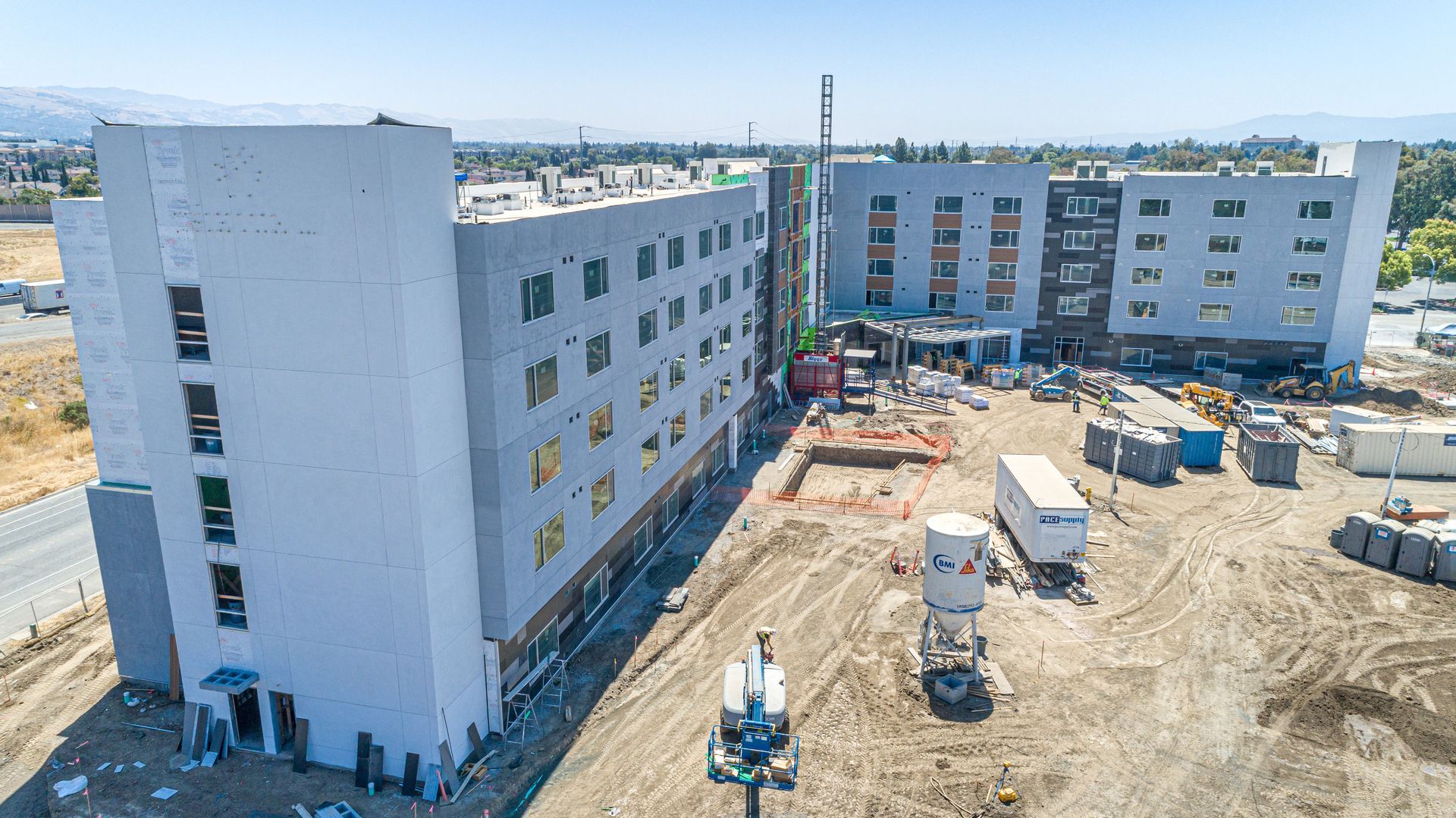 Construction site with white apartment buildings and heavy equipment in a dirt lot