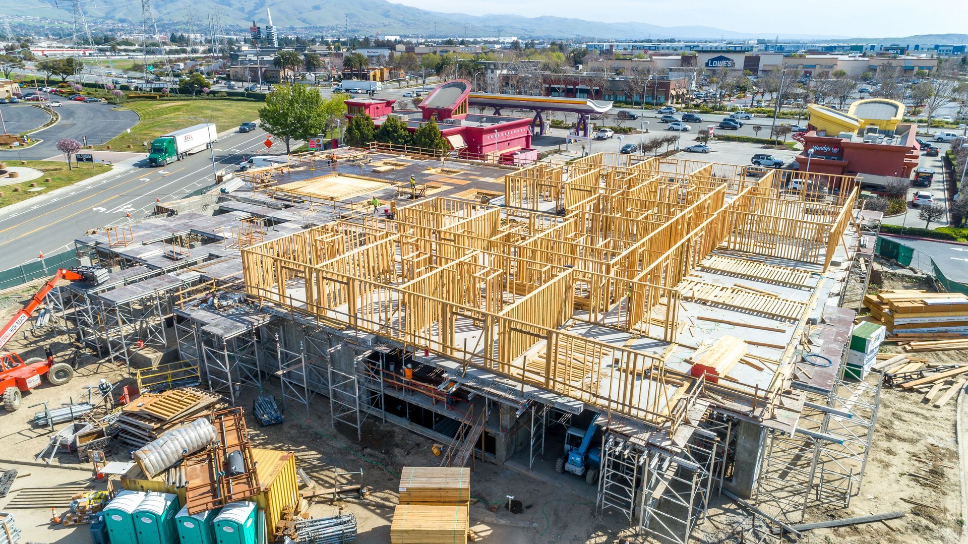 Aerial view of a large wooden building under construction with cranes and surrounding city streets.