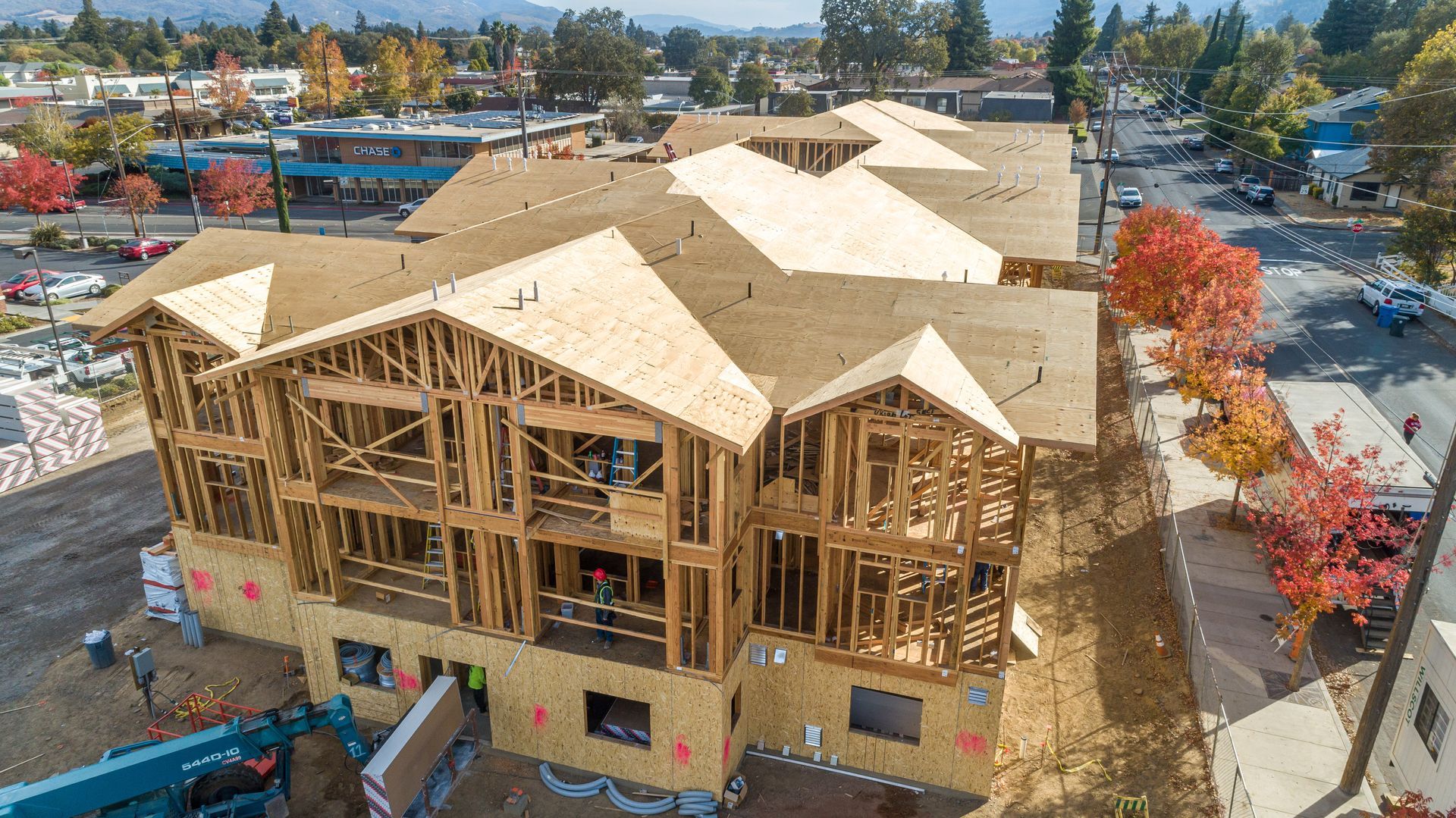 Wood-framed house under construction with tan roof sheathing on a residential lot