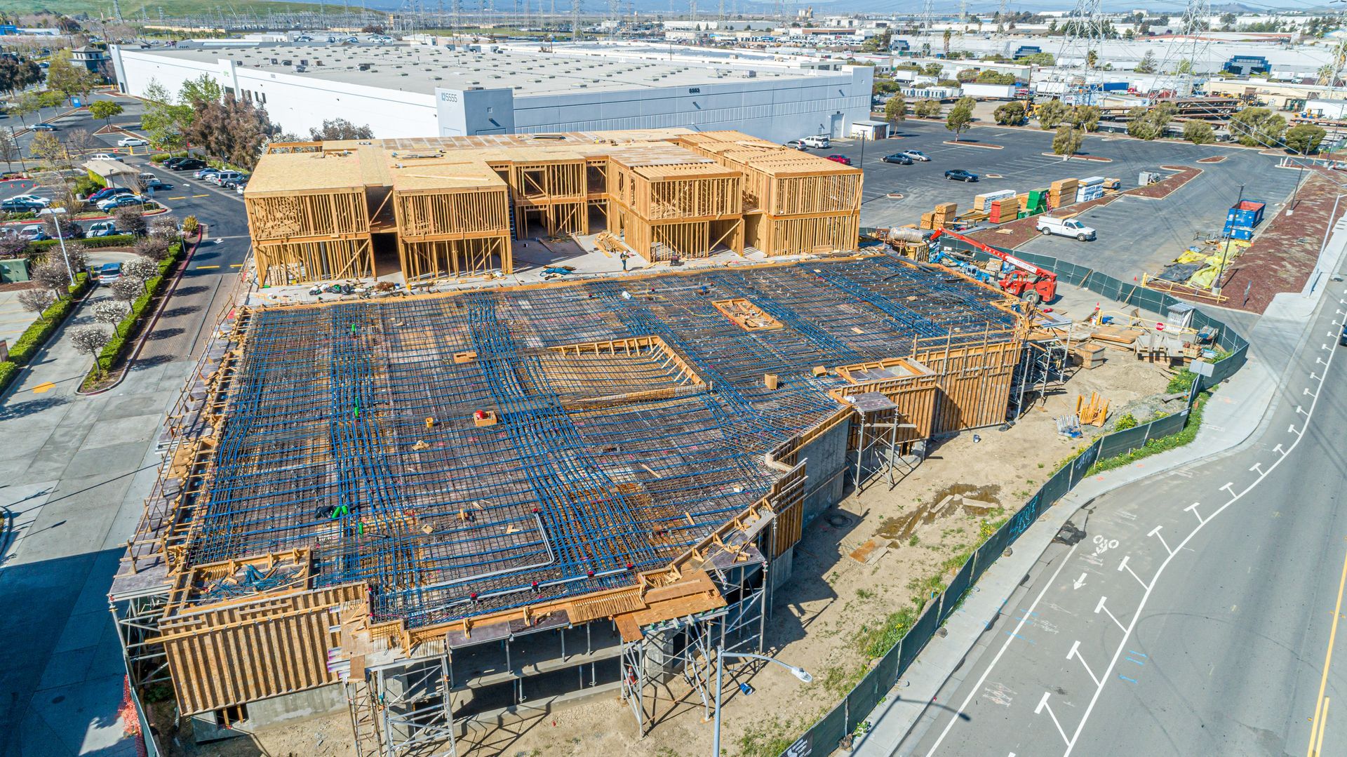 Aerial view of a large construction site with a wood-framed building and road beside it