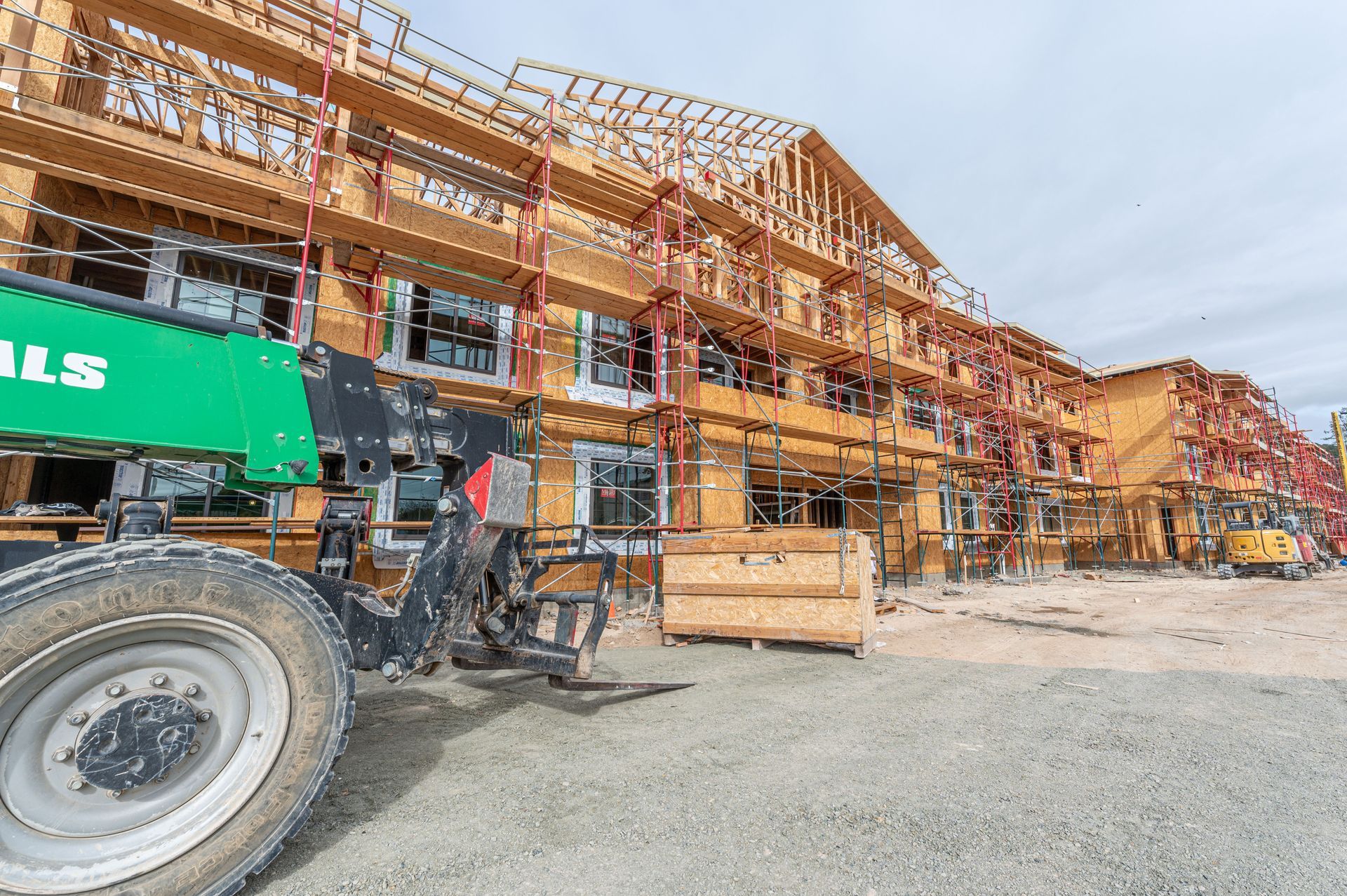 Construction site with a wooden-framed building, green machinery, and workers on gravel road