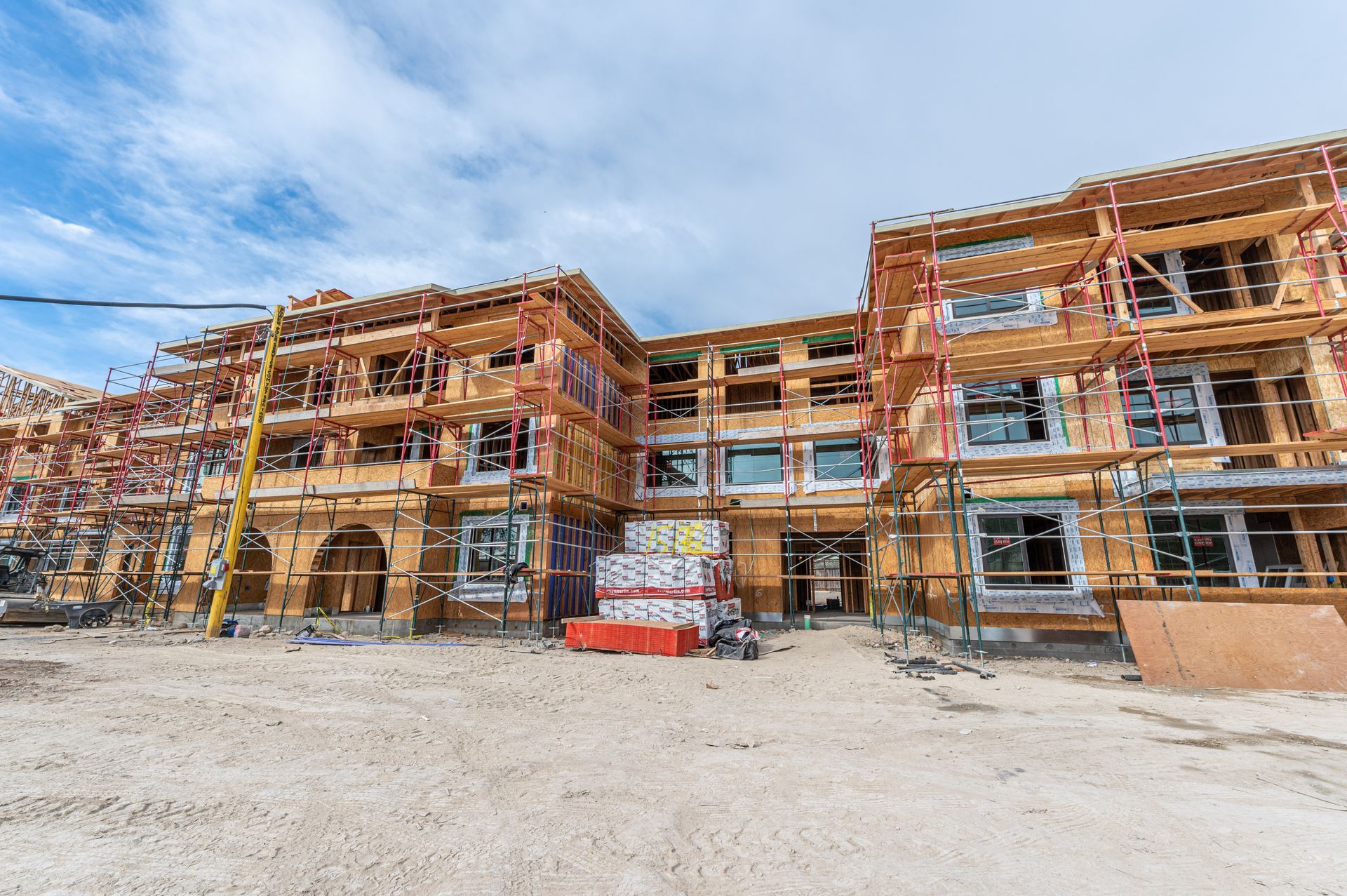 Construction site with a multi-story building under construction, wood framing and scaffolding against a blue sky