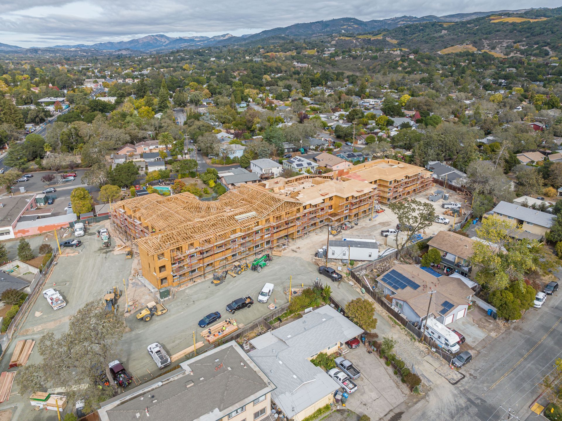 Aerial view of a large wooden building under construction in a suburban neighborhood with hills in the distance