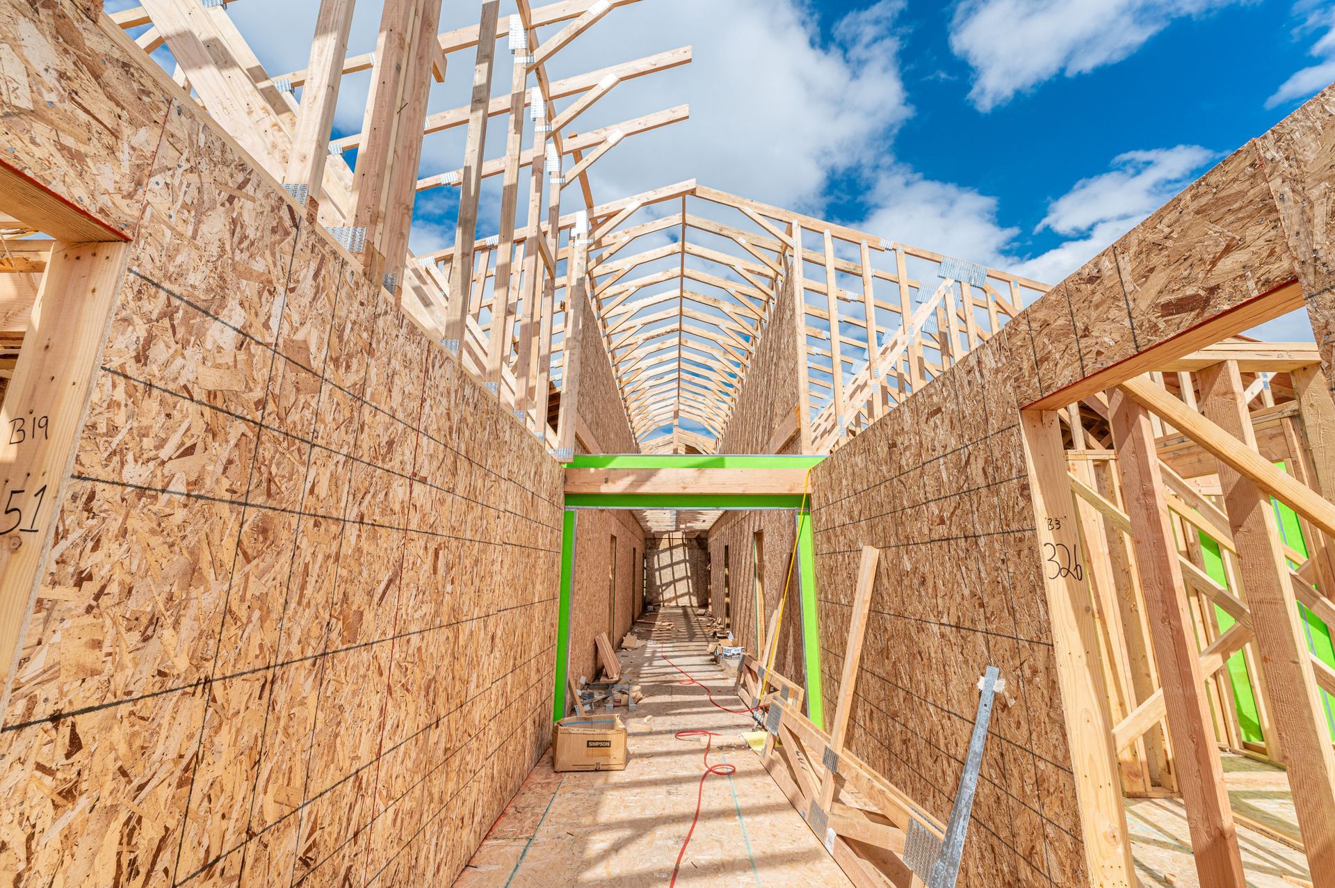 Partially built wooden house framing under a bright blue sky with green construction tape accents