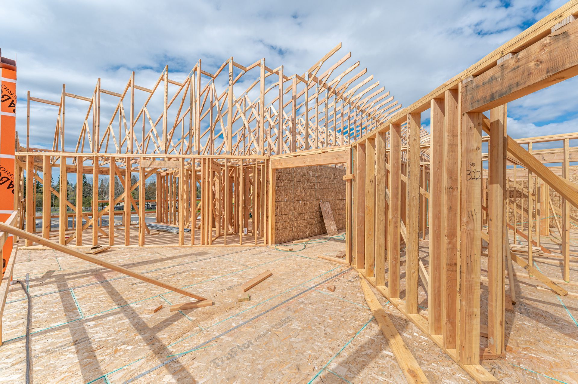 Wood-framed house under construction with exposed roof trusses against a blue sky