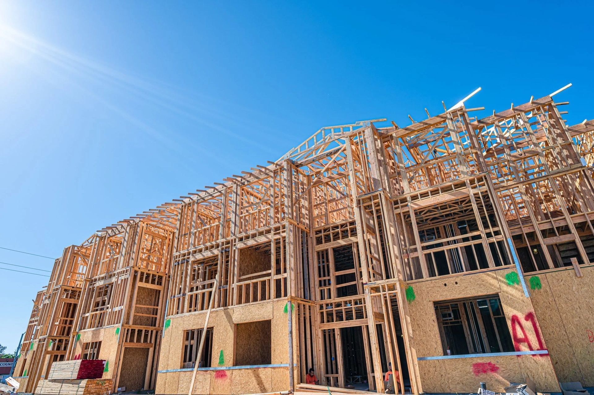 A multi-story residential building under construction, featuring an exposed wooden frame against a bright blue sky.