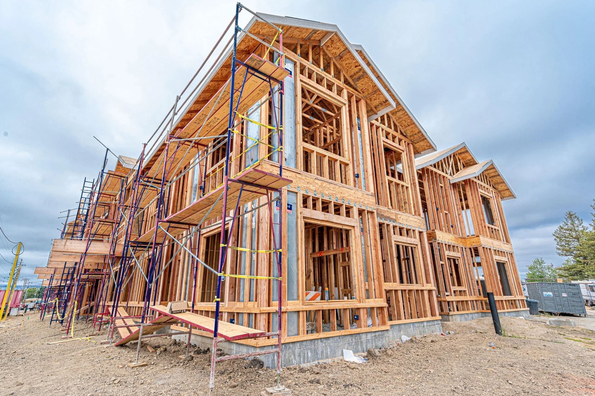 A multi-story residential building under construction with exposed wooden framing and scaffolding against a cloudy sky.