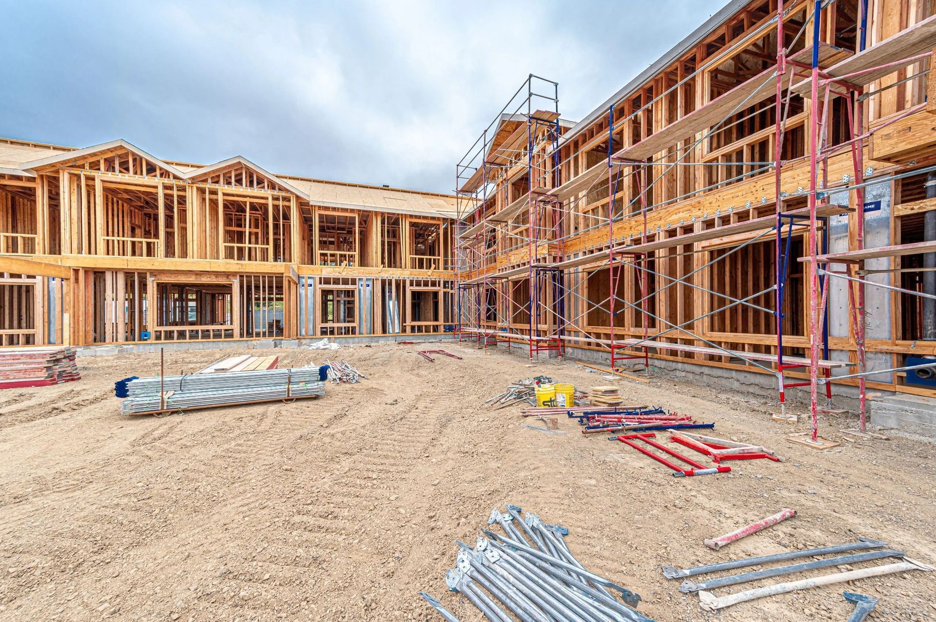 A multi-story wooden apartment complex under construction with scaffolding, building materials, and a dirt ground.