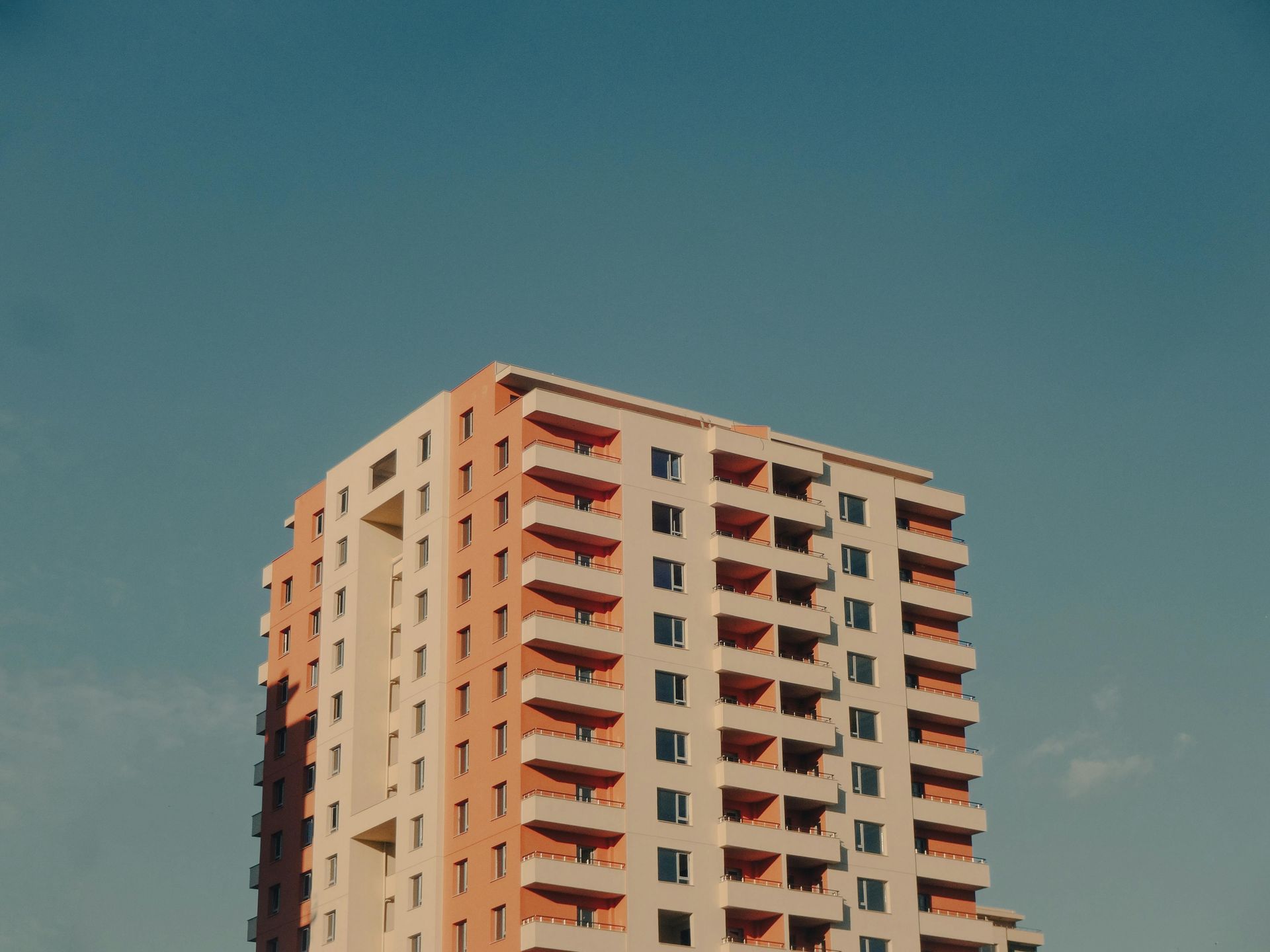 A high-rise residential building with peach-colored and white walls against a clear blue sky.