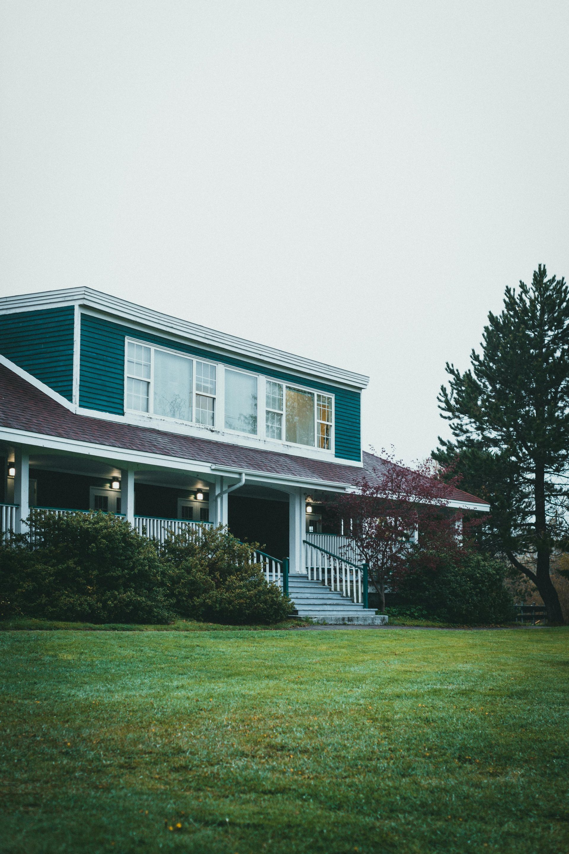 A teal house with a brown metal roof sits behind a green lawn under a grey.
