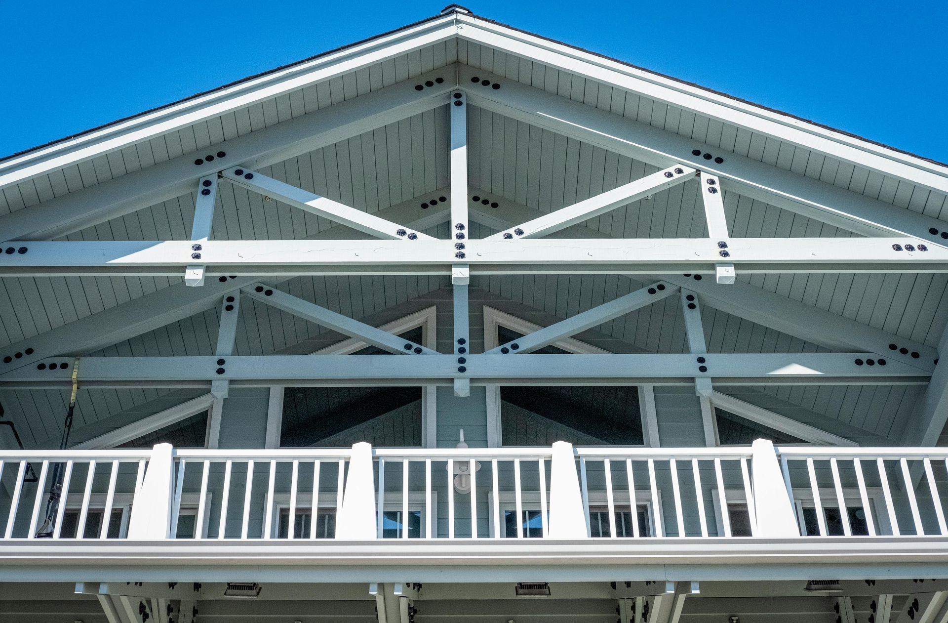 A white timber-framed gable roof structure with a balcony against a clear blue sky.