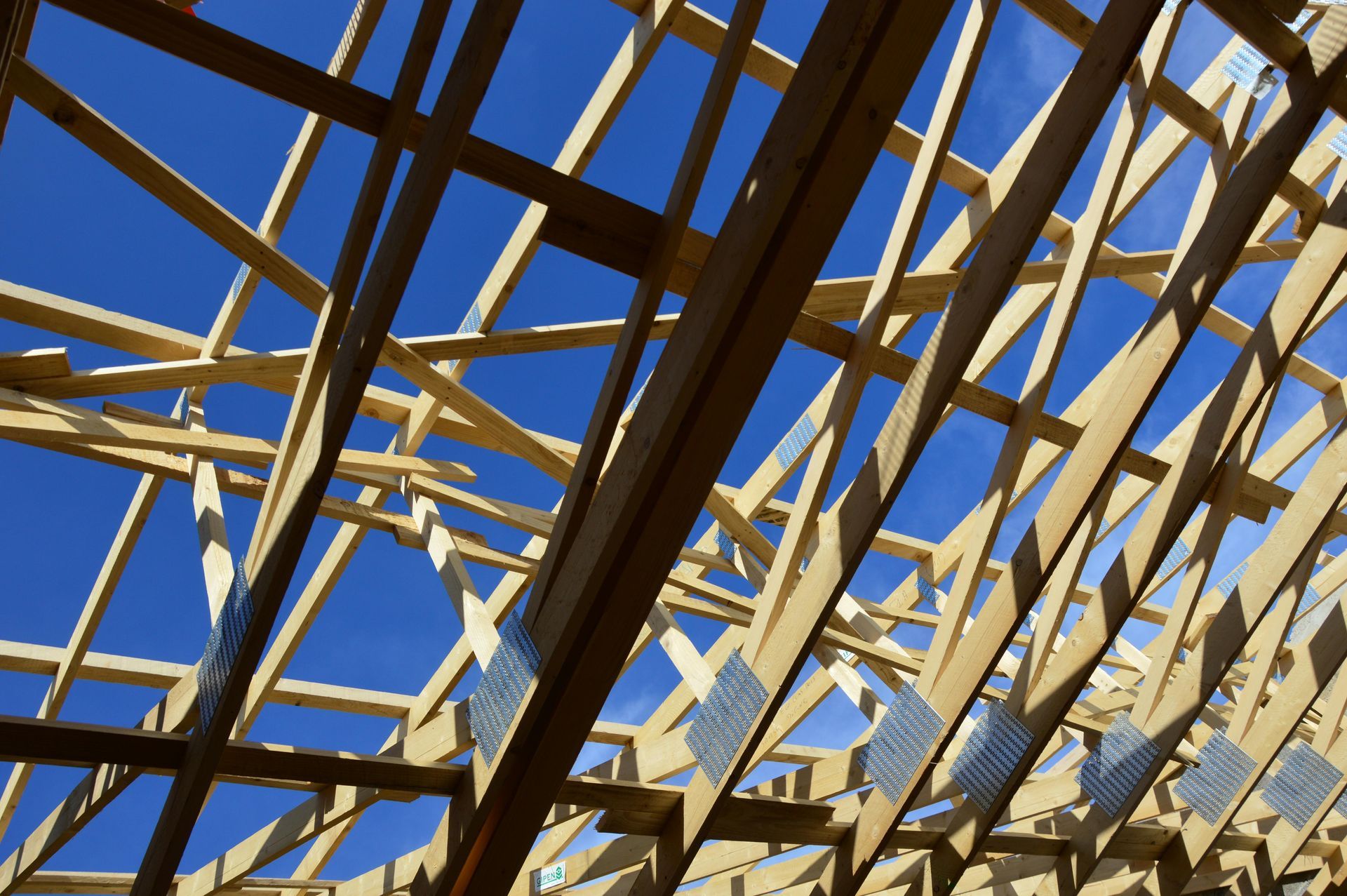 Wooden roof trusses under construction against a clear blue sky.
