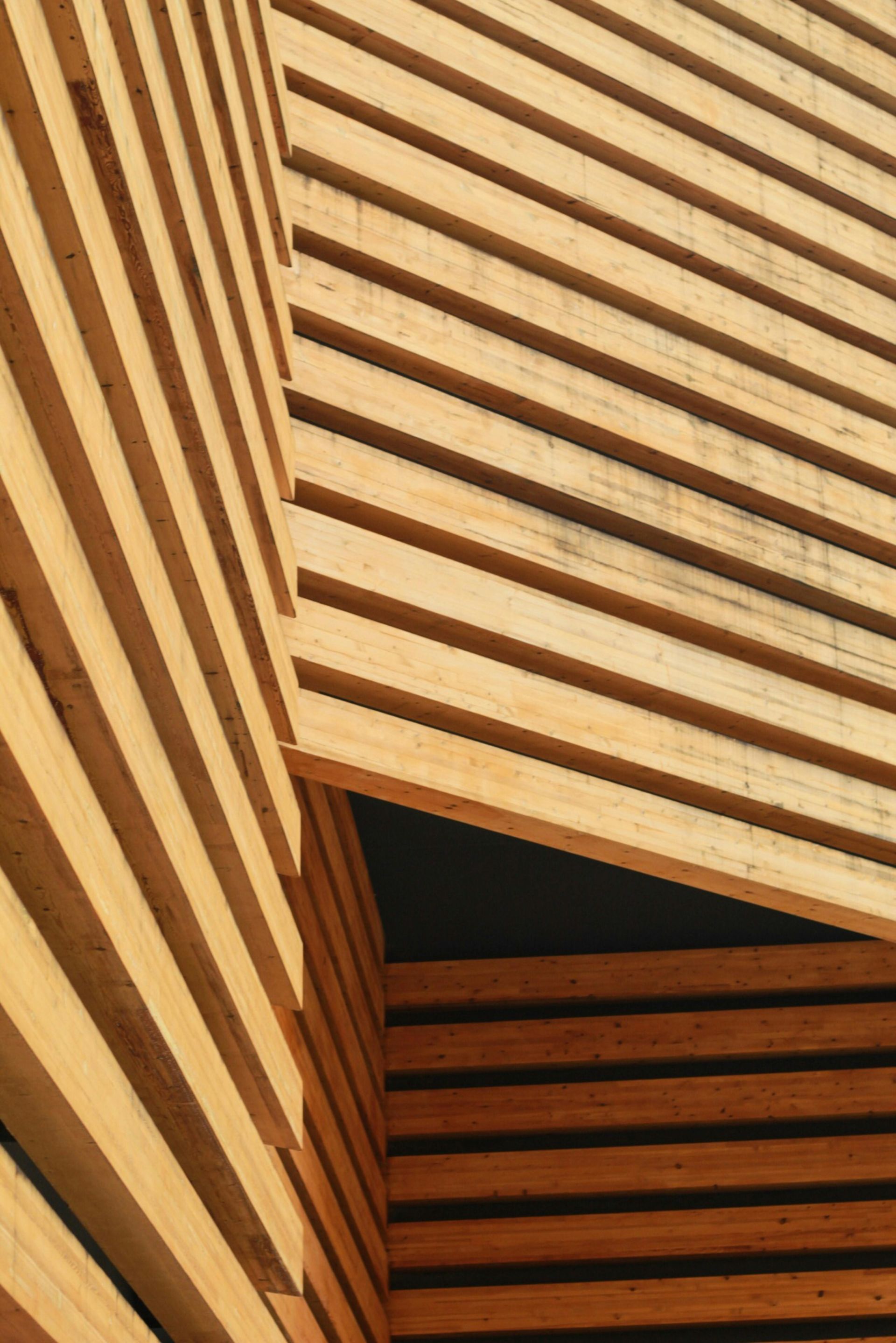An architectural detail of light-colored, horizontal wooden slats forming a corner and an angled overhang.