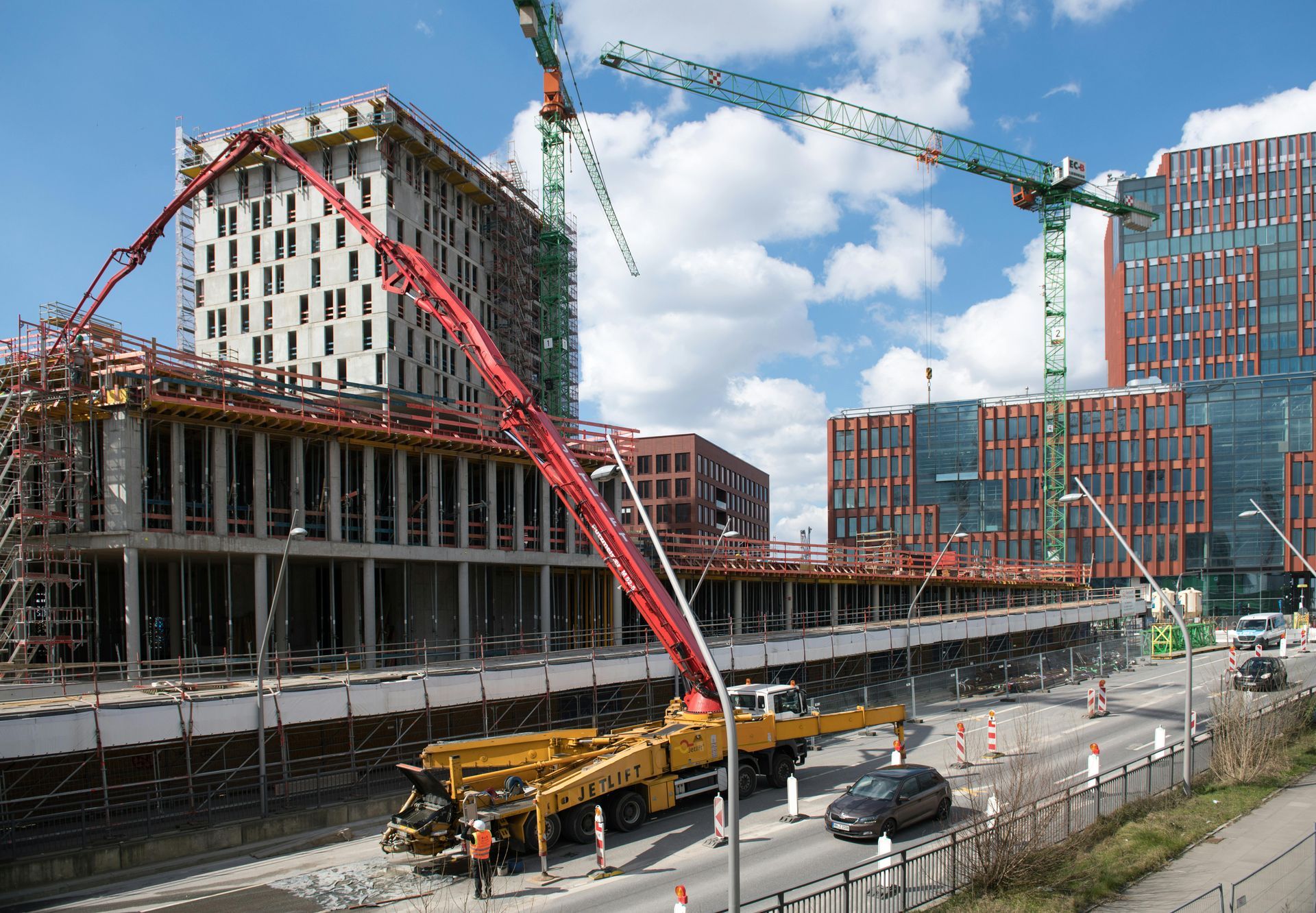 A construction site with a yellow concrete pump truck extending its long arm over an unfinished building.