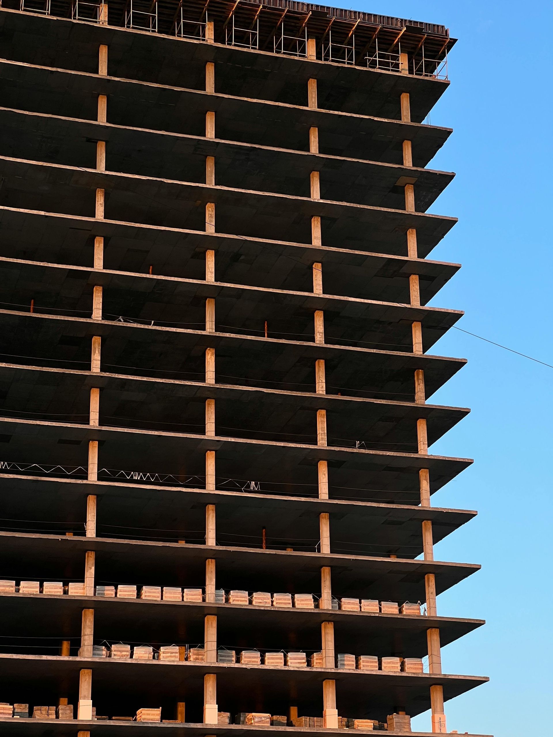 A partially constructed concrete high-rise building with exposed floors against a clear blue sky.