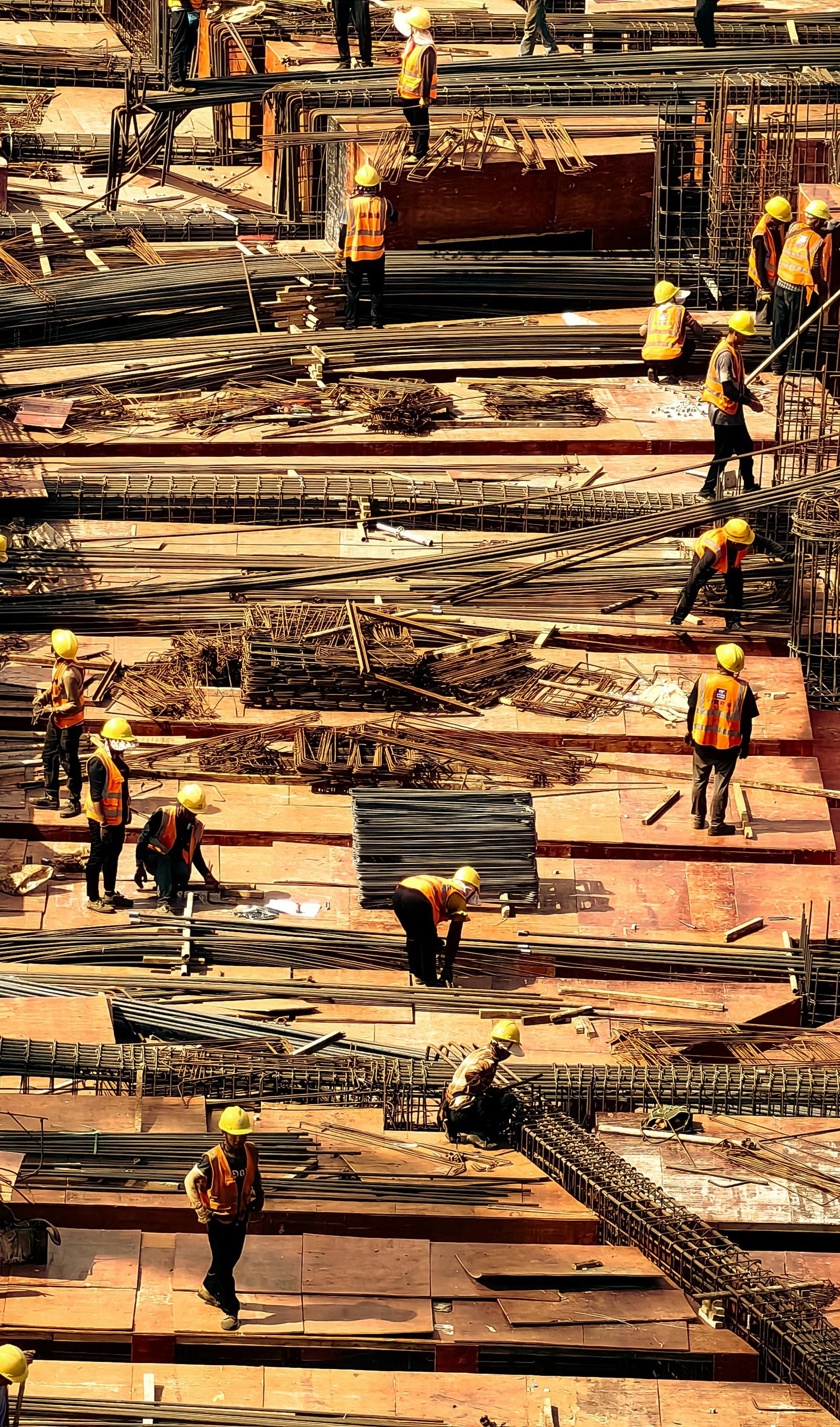 Construction workers in safety vests and hard hats install steel rebar on a building site.