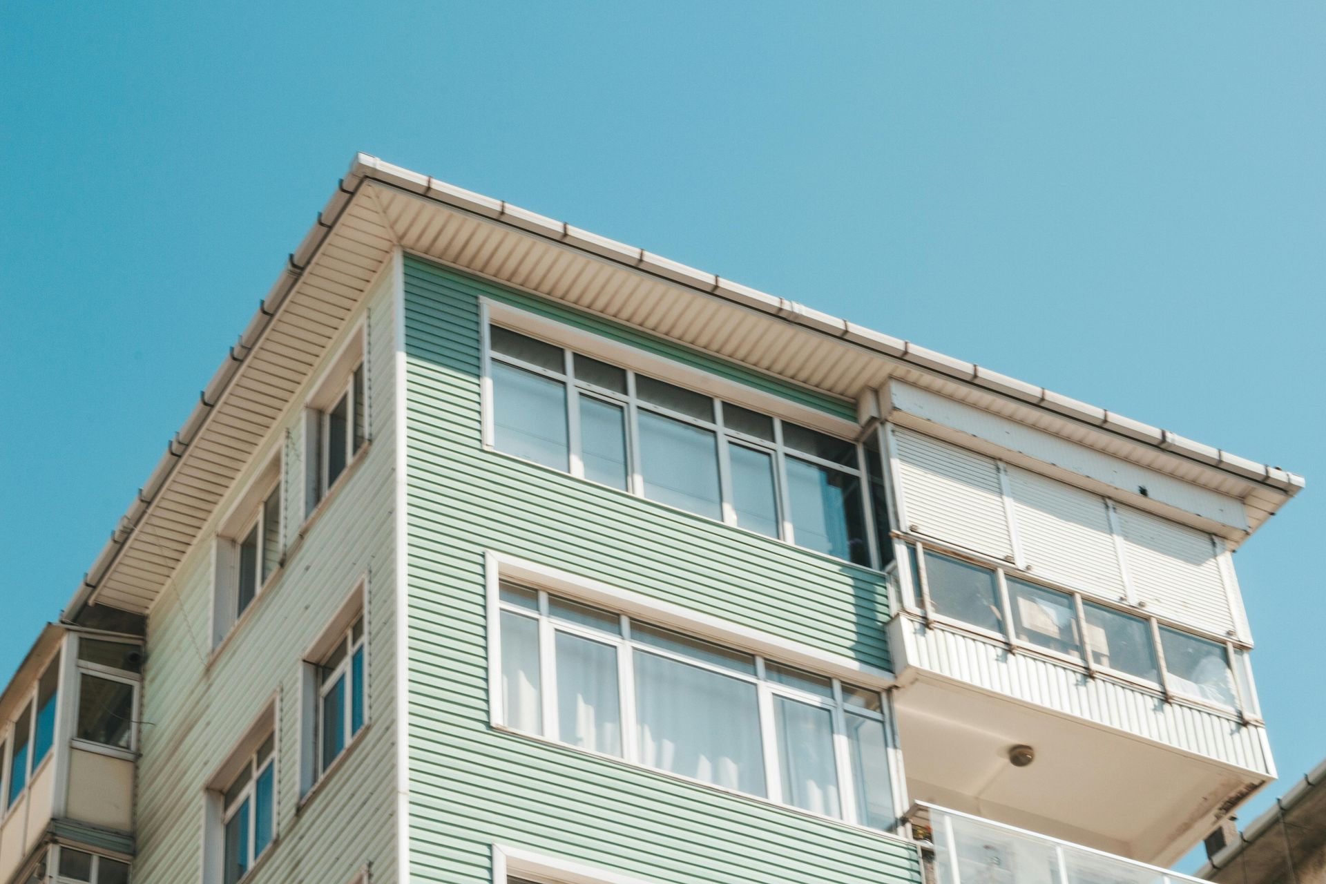A low-angle view of a multi-story apartment building with light green siding and a white overhang.