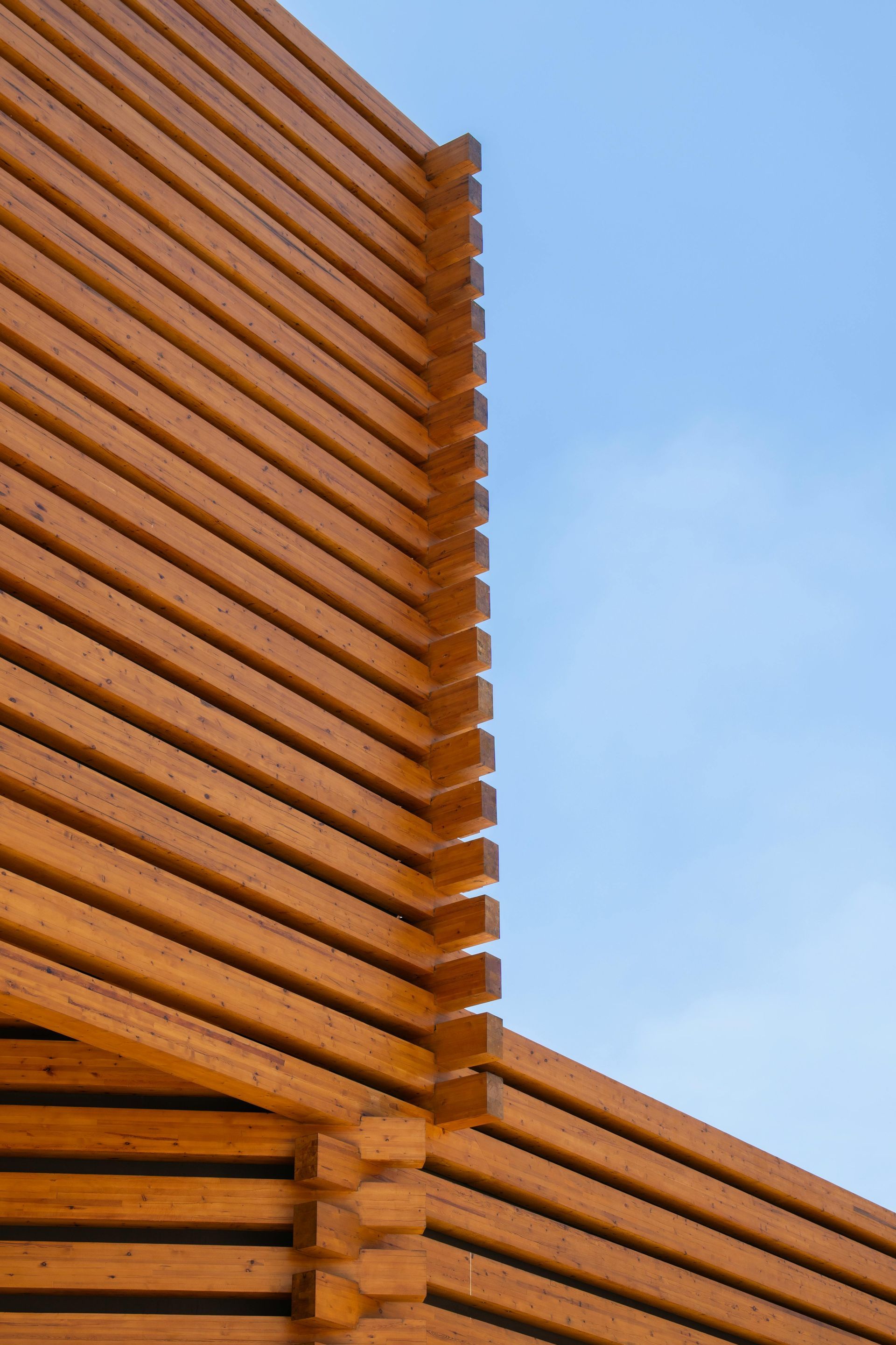 A corner detail of a building exterior made from horizontal stacked wooden beams against a clear blue sky.