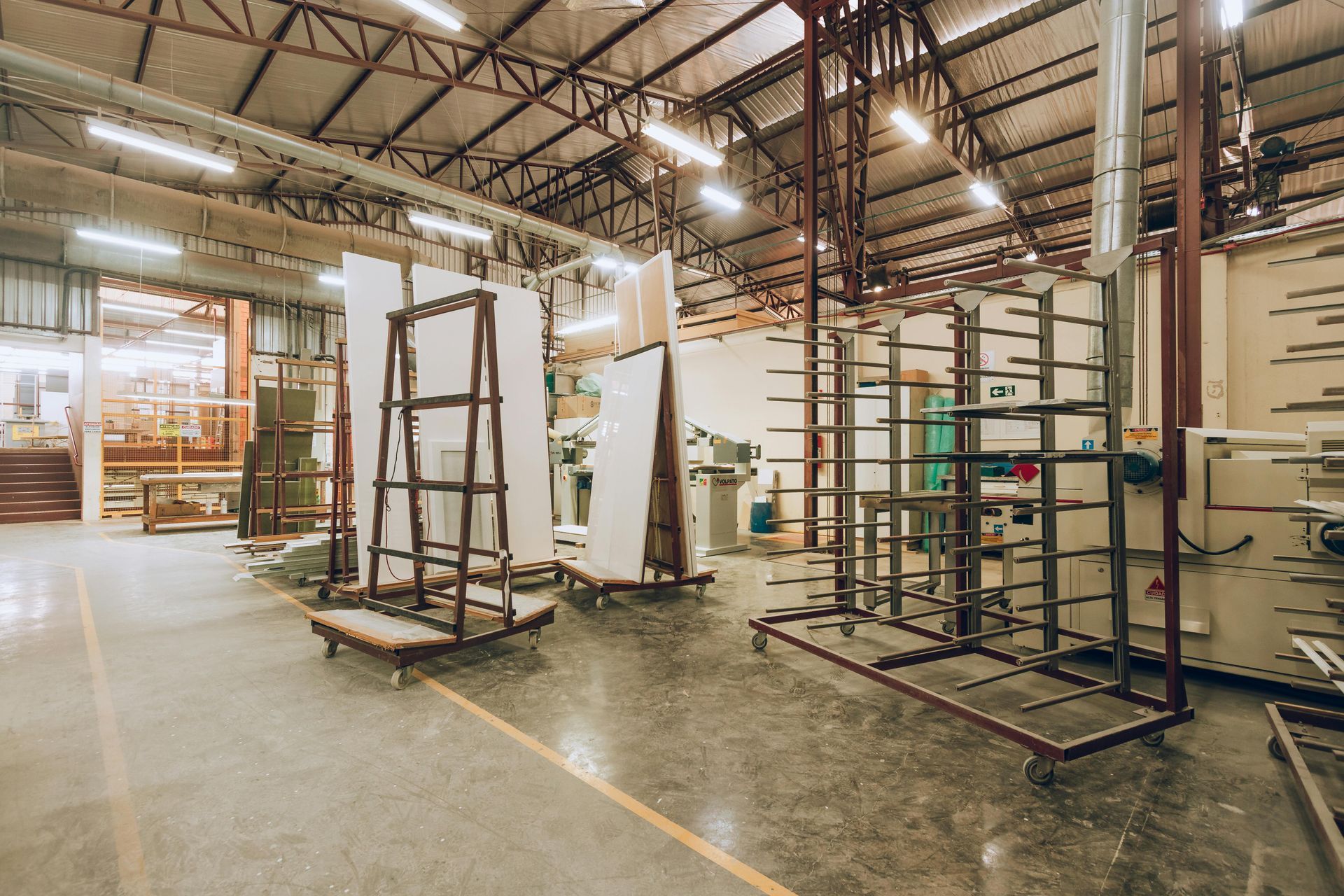 A spacious workshop featuring metal racks and carts used for storing large panels and materials under high ceilings.