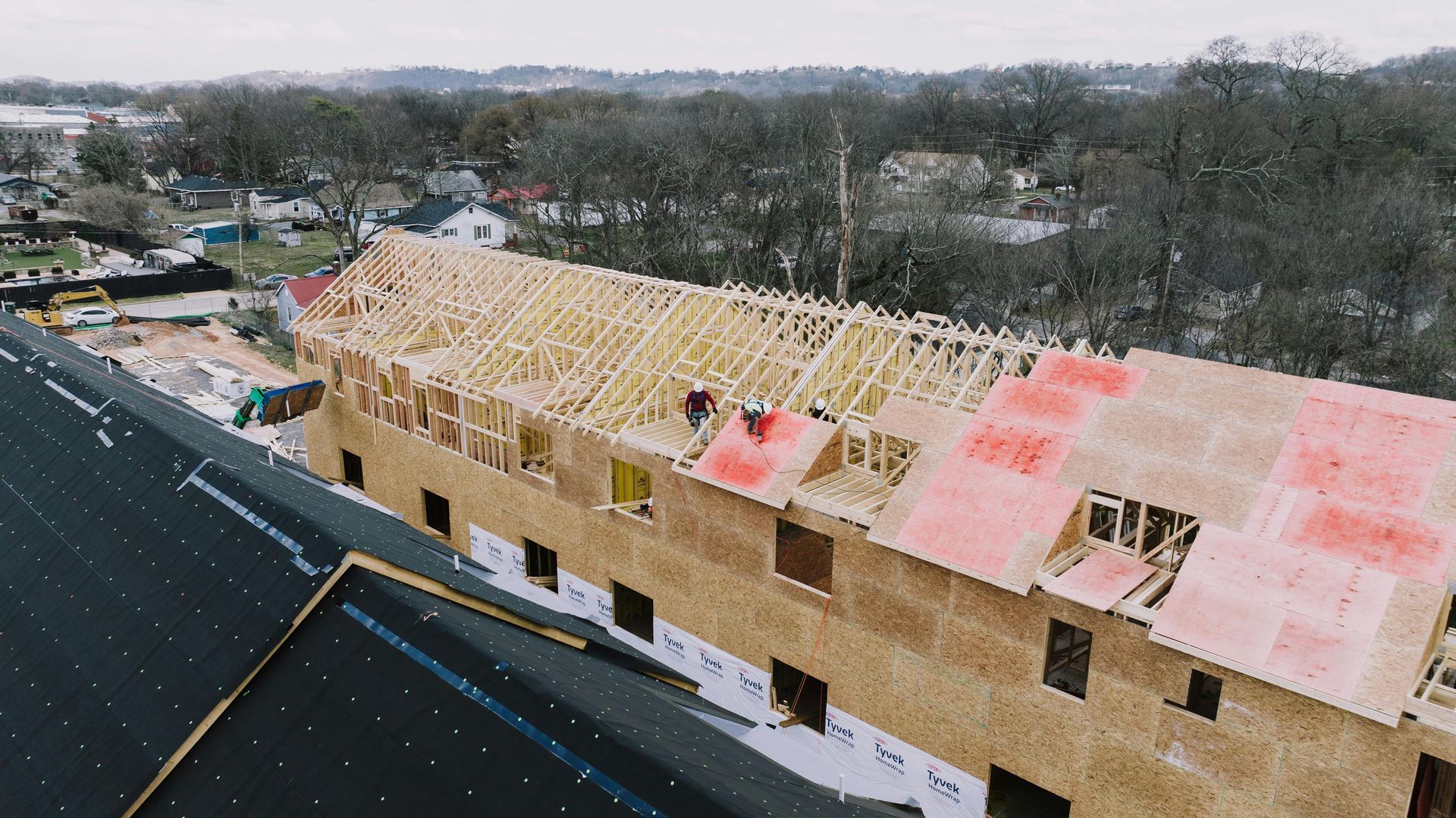 A high-angle view of construction workers installing wooden roof trusses and sheathing on a multi-story building.