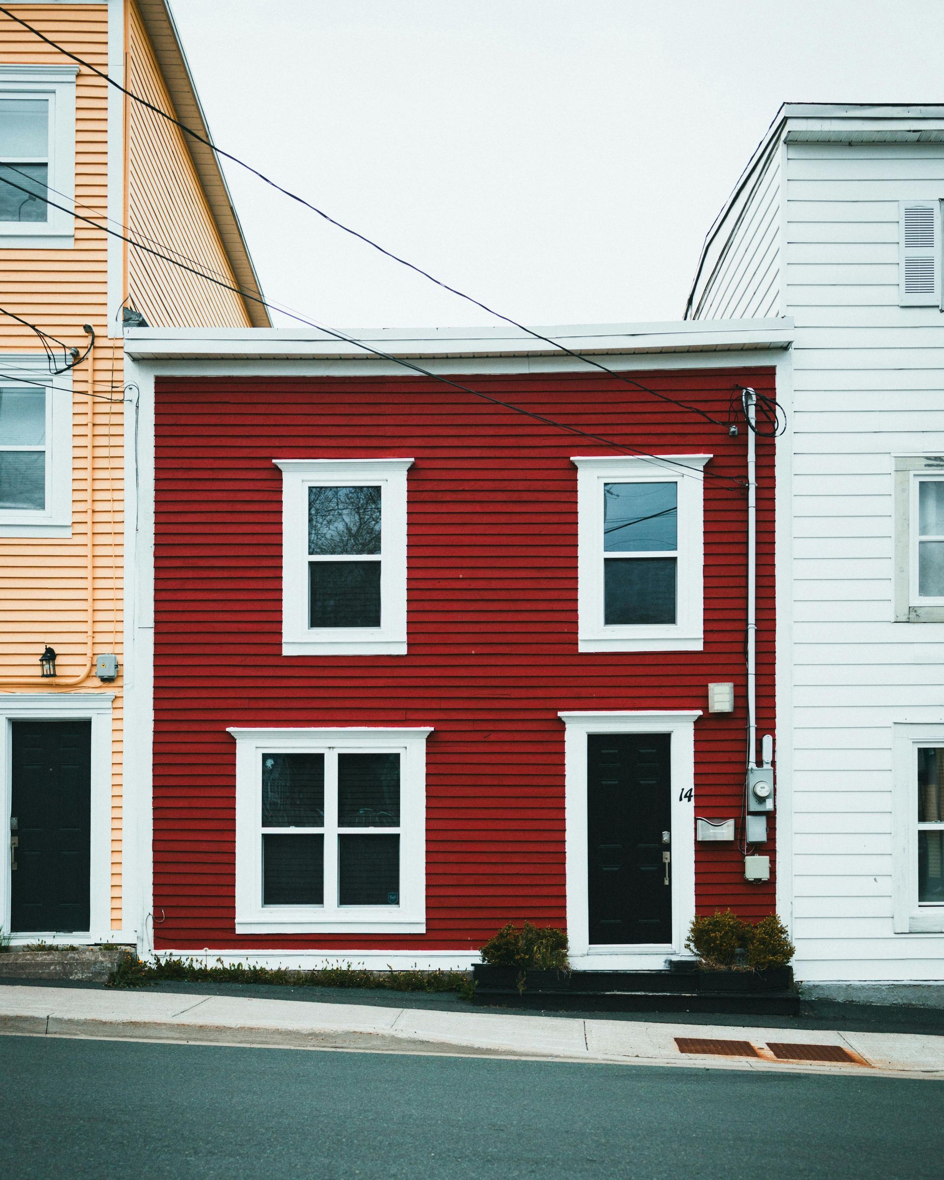 A row of three narrow houses in yellow, red, and white, viewed from the street.