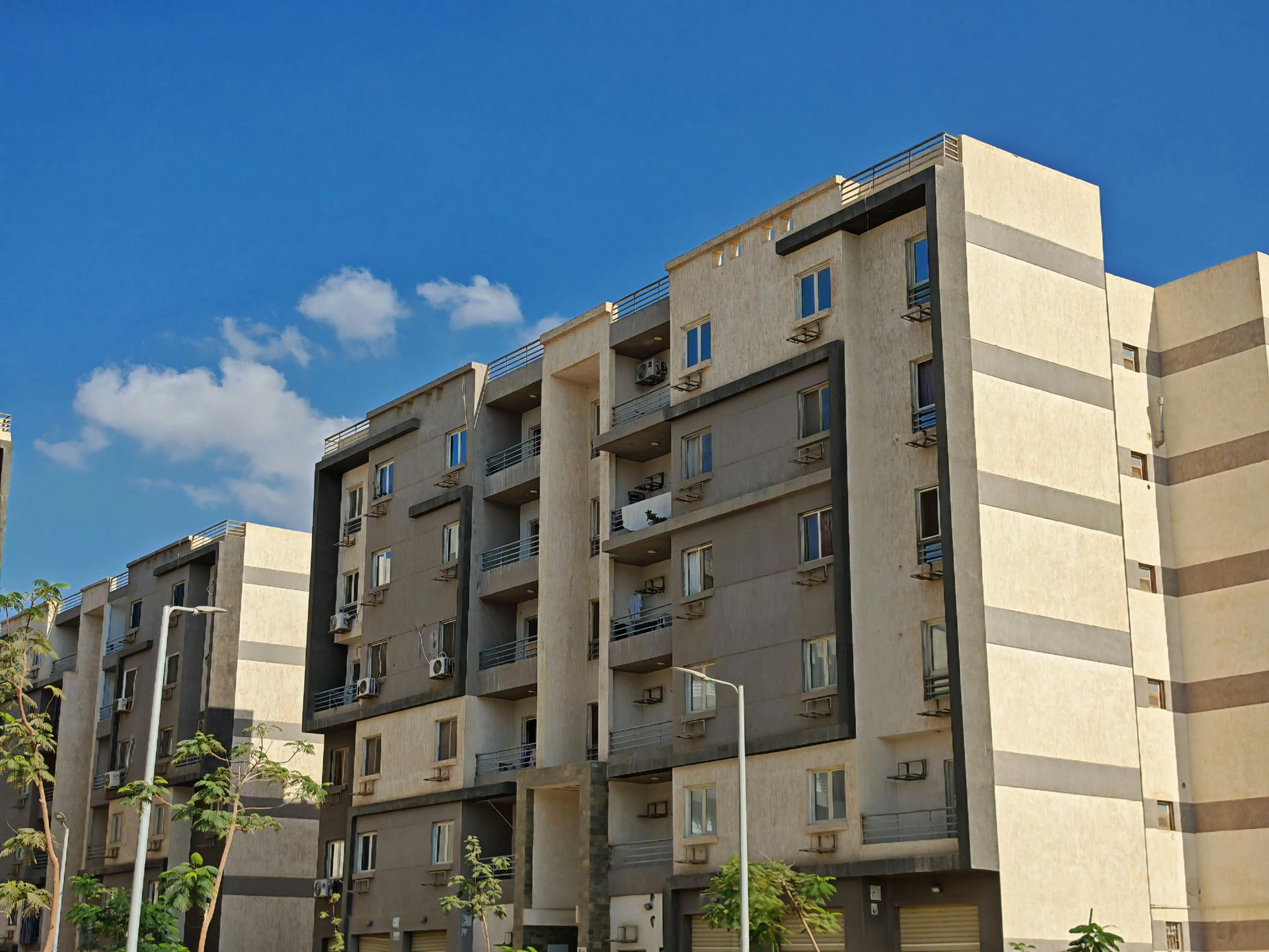 A multi-story modern residential apartment building with light and dark beige paneling under a clear blue sky.