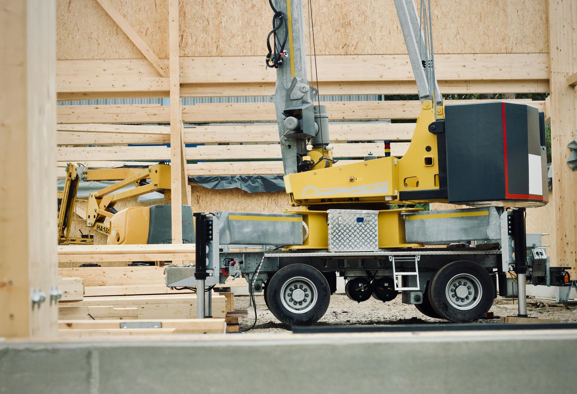 A yellow crane and a construction vehicle parked at a wooden building site.