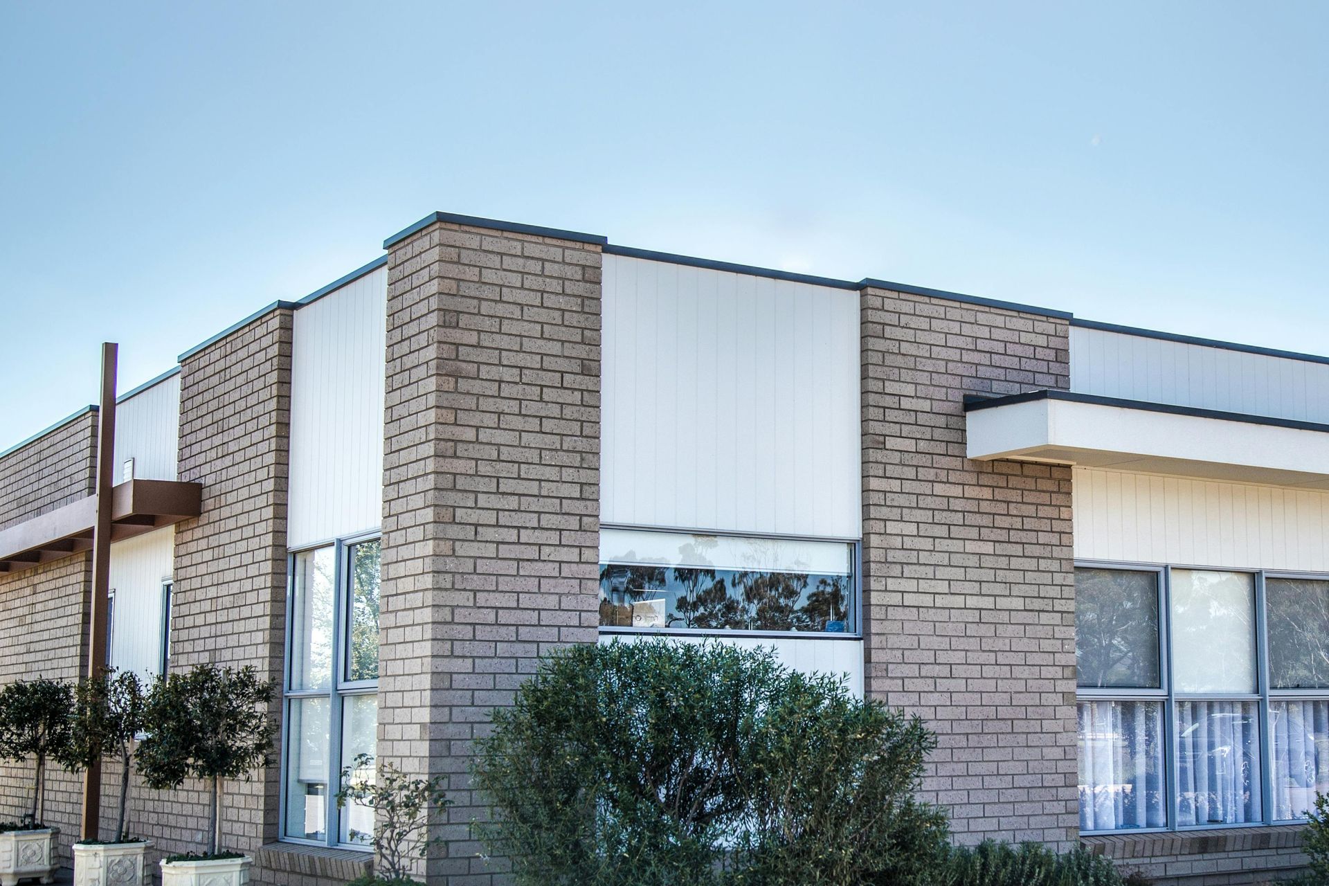 A low-rise building featuring light-colored brick walls, white vertical panels, and large glass windows.