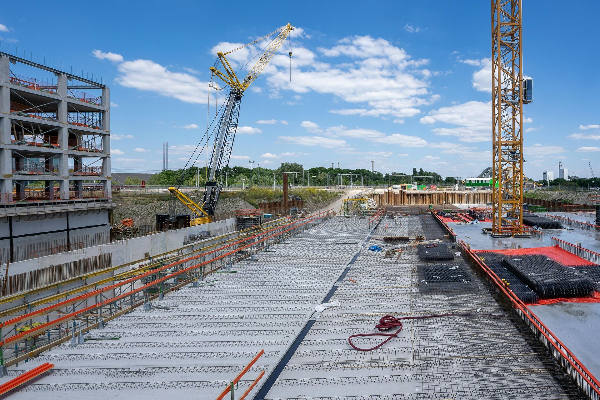 A wide-angle shot of a construction site featuring a concrete foundation, a yellow crane, and a partially built structure.