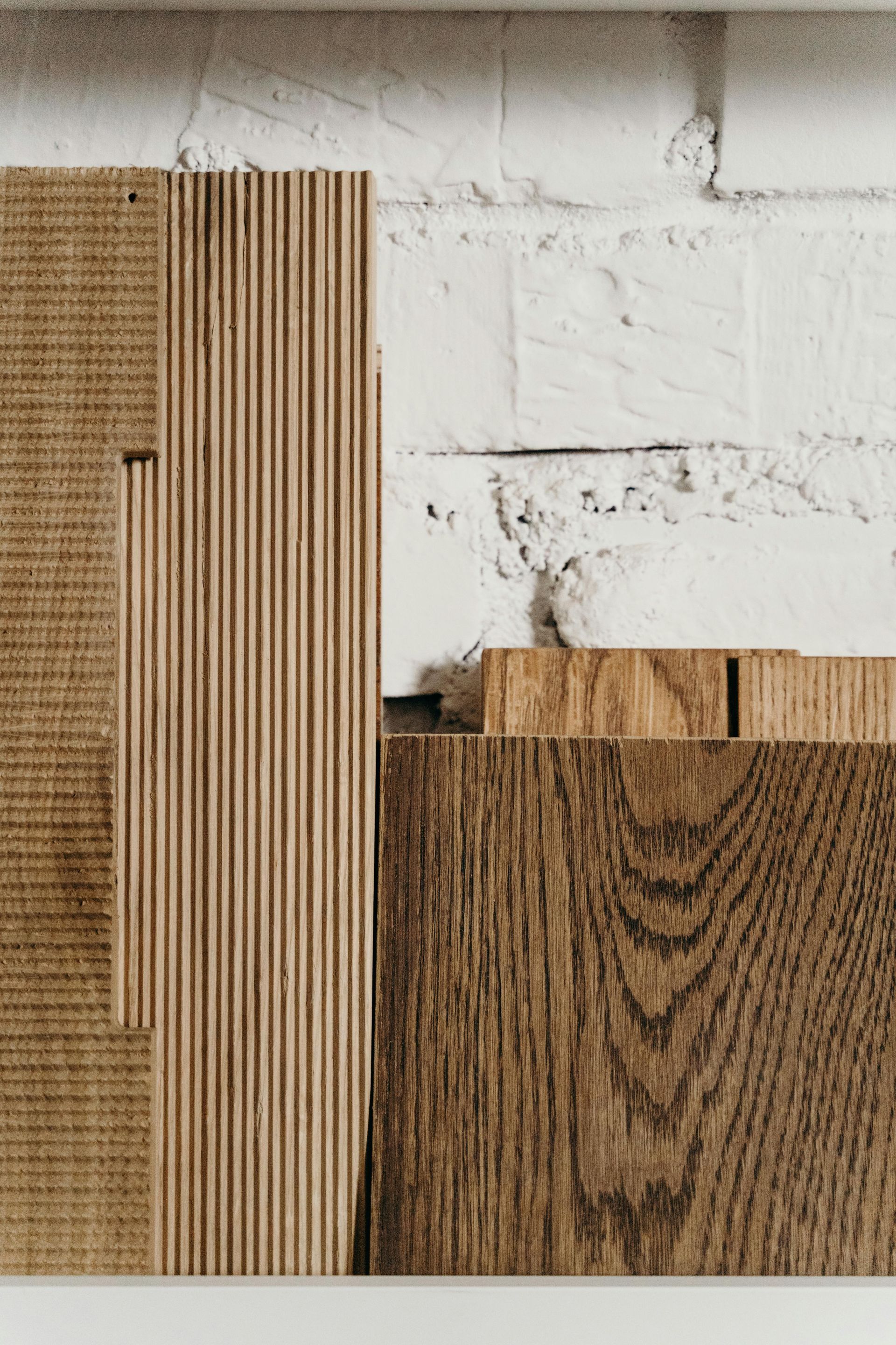 Samples of plywood showing layered edges and a piece of textured wood grain against a white brick wall.