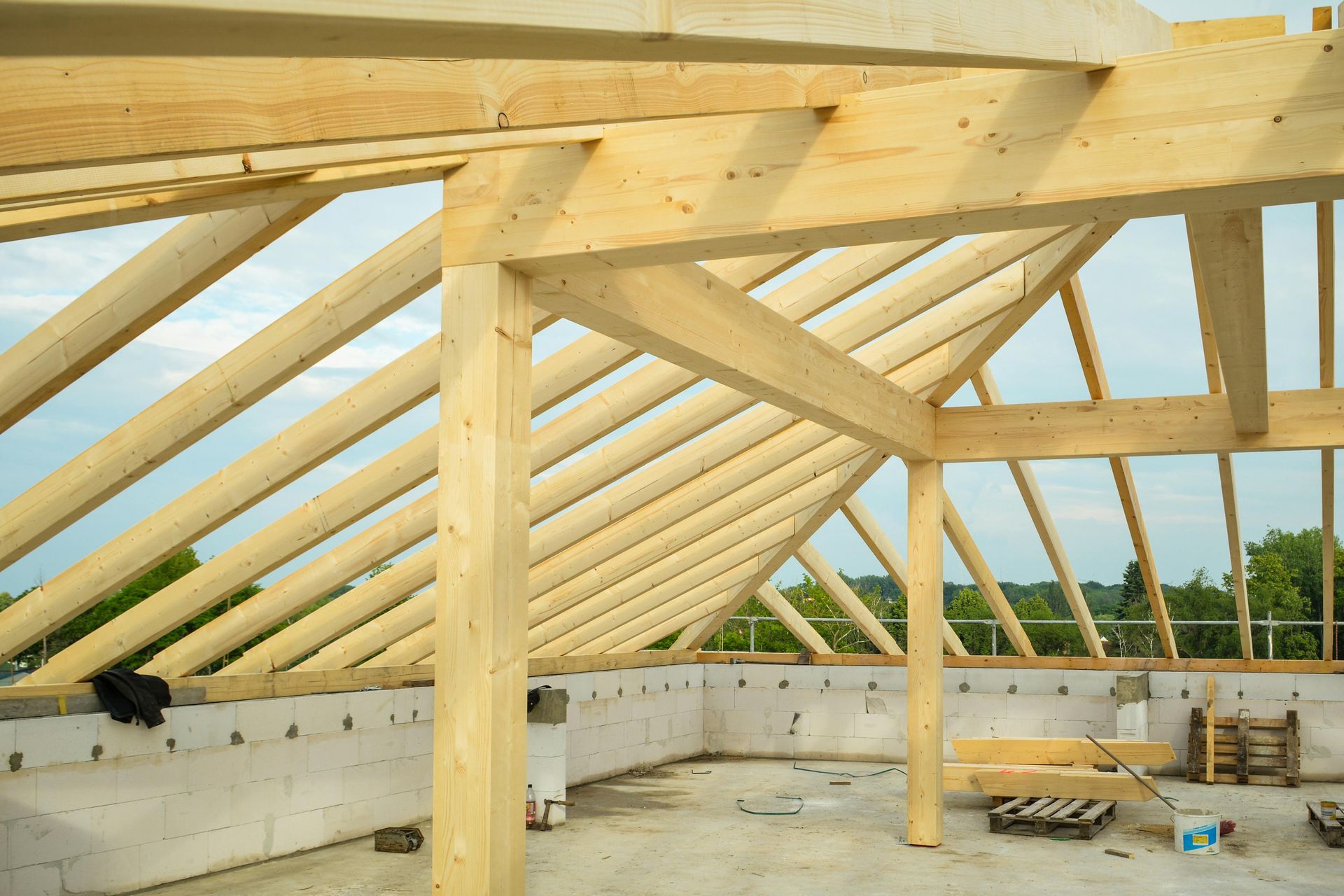 A wooden roof frame under construction, featuring rafters and support beams resting on cinder block walls.