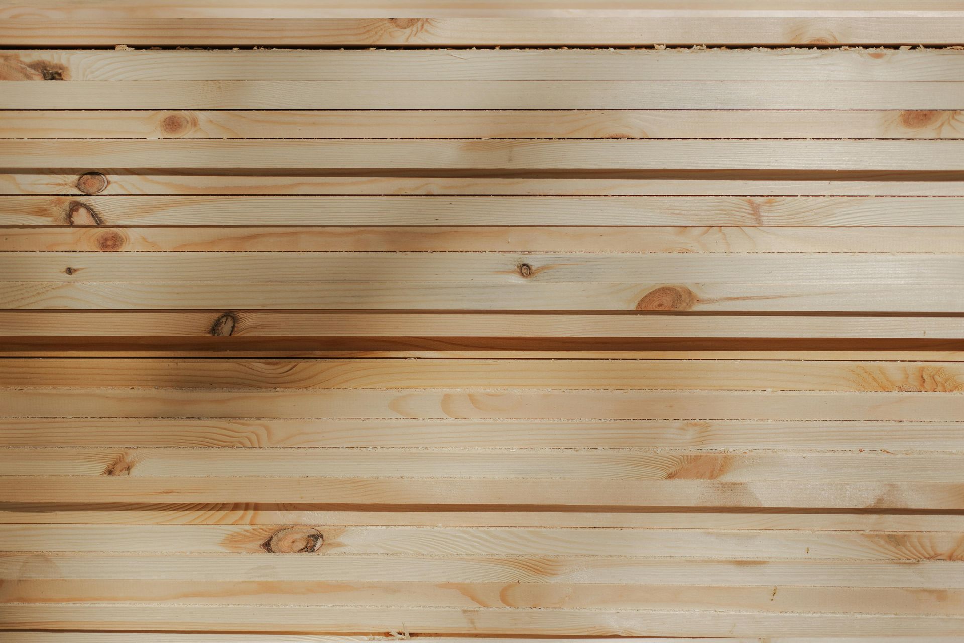 A stacked pile of light-colored, natural wood planks with visible grain and knots.