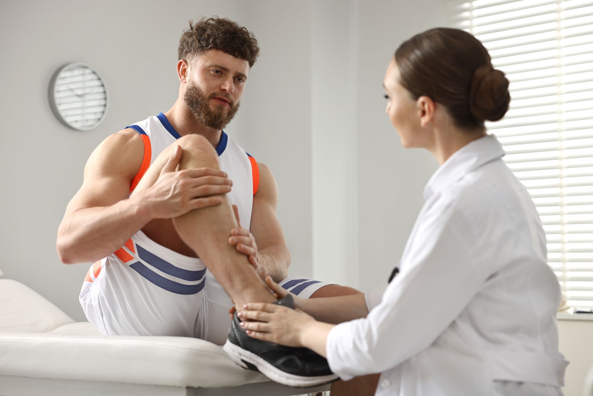 A man is sitting on a table while a female doctor examines his knee.