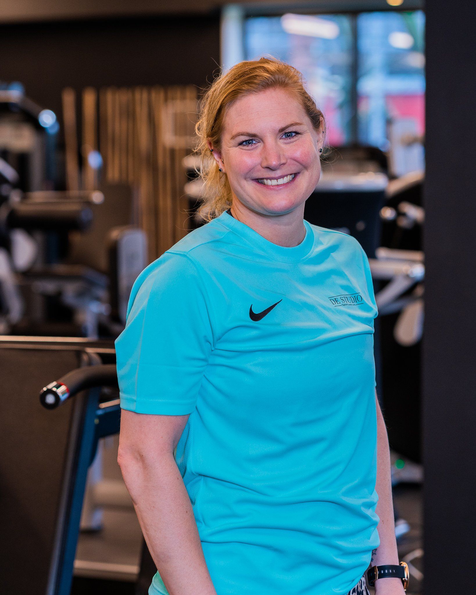 Een vrouw in een blauw Nike-shirt lacht in een sportschool.