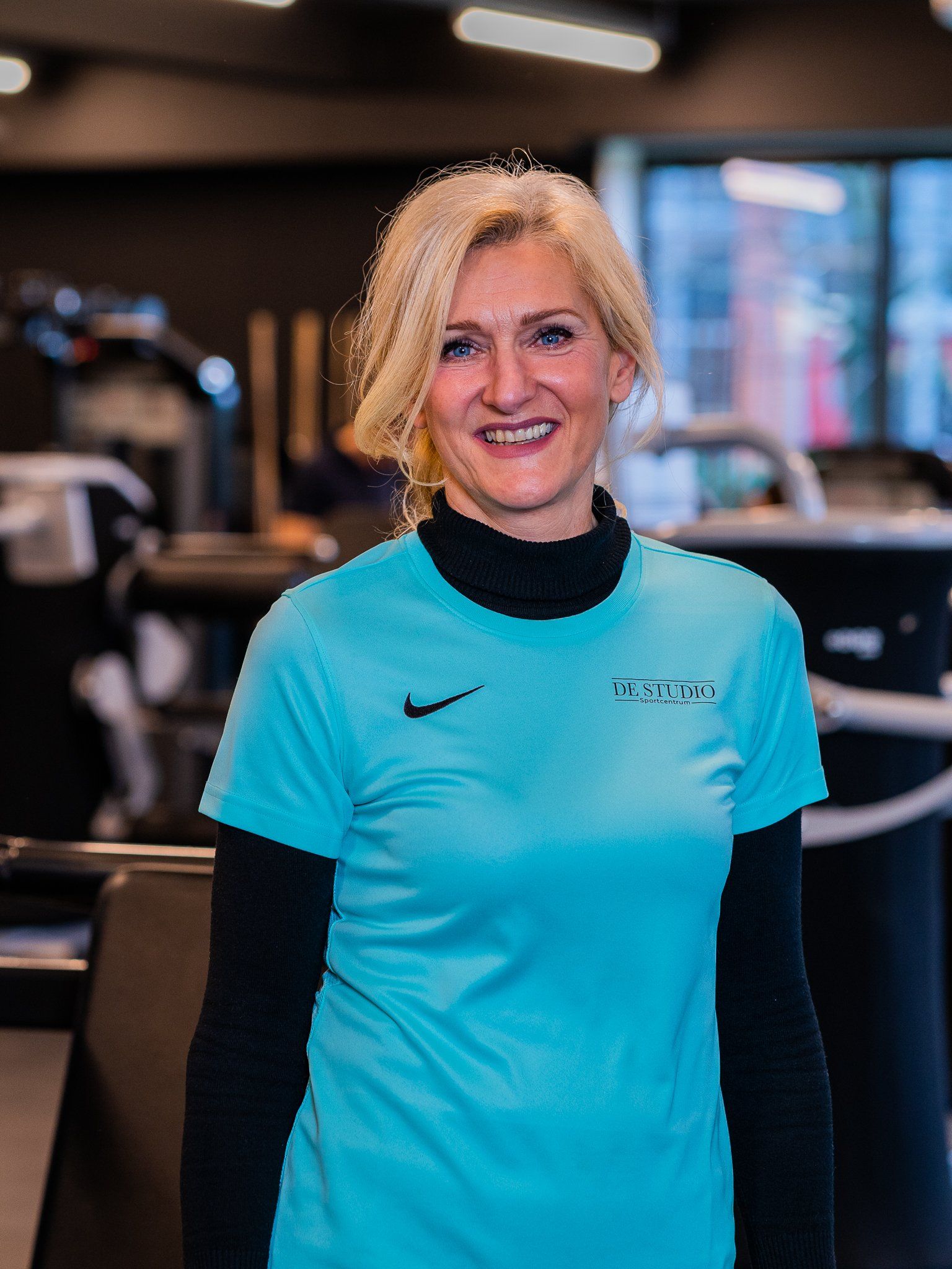 Een vrouw in een blauw Nike-shirt lacht in een sportschool.