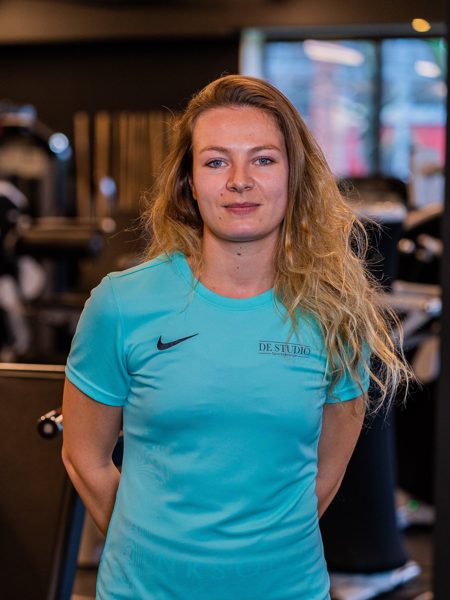 Een vrouw in een blauw shirt staat in een sportschool.