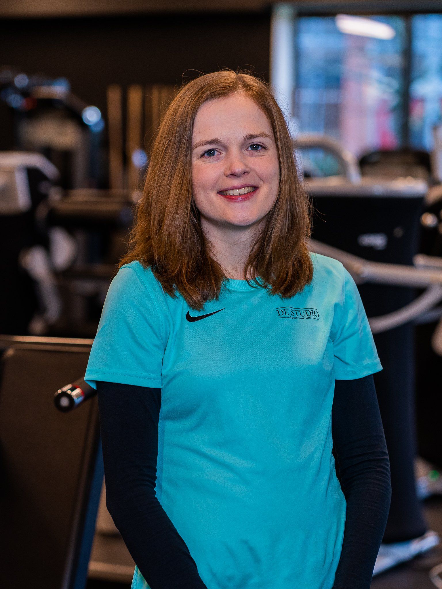 Een vrouw in een blauw shirt lacht in een sportschool.