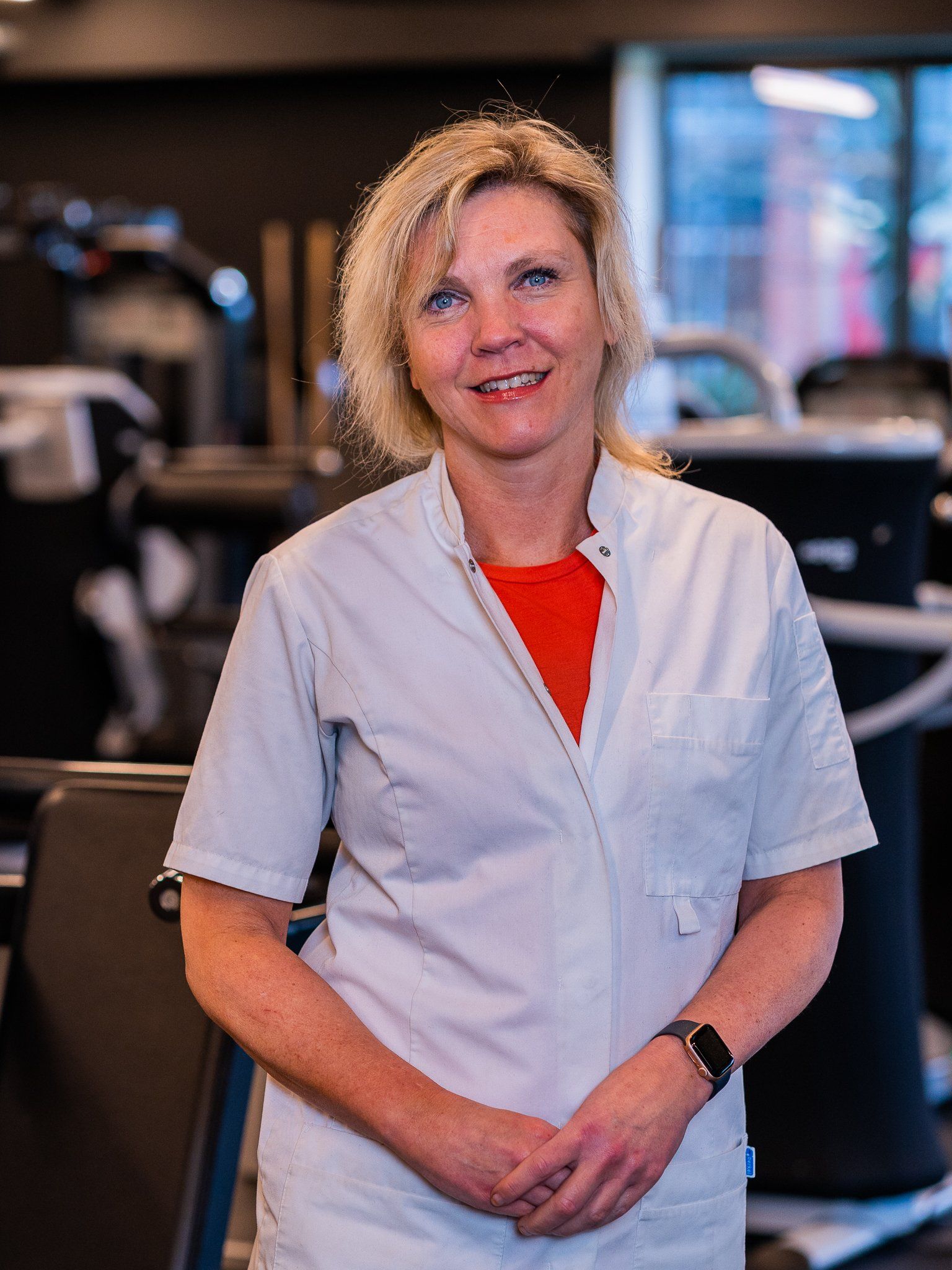 Een vrouw in een witte laboratoriumjas staat in een sportschool.