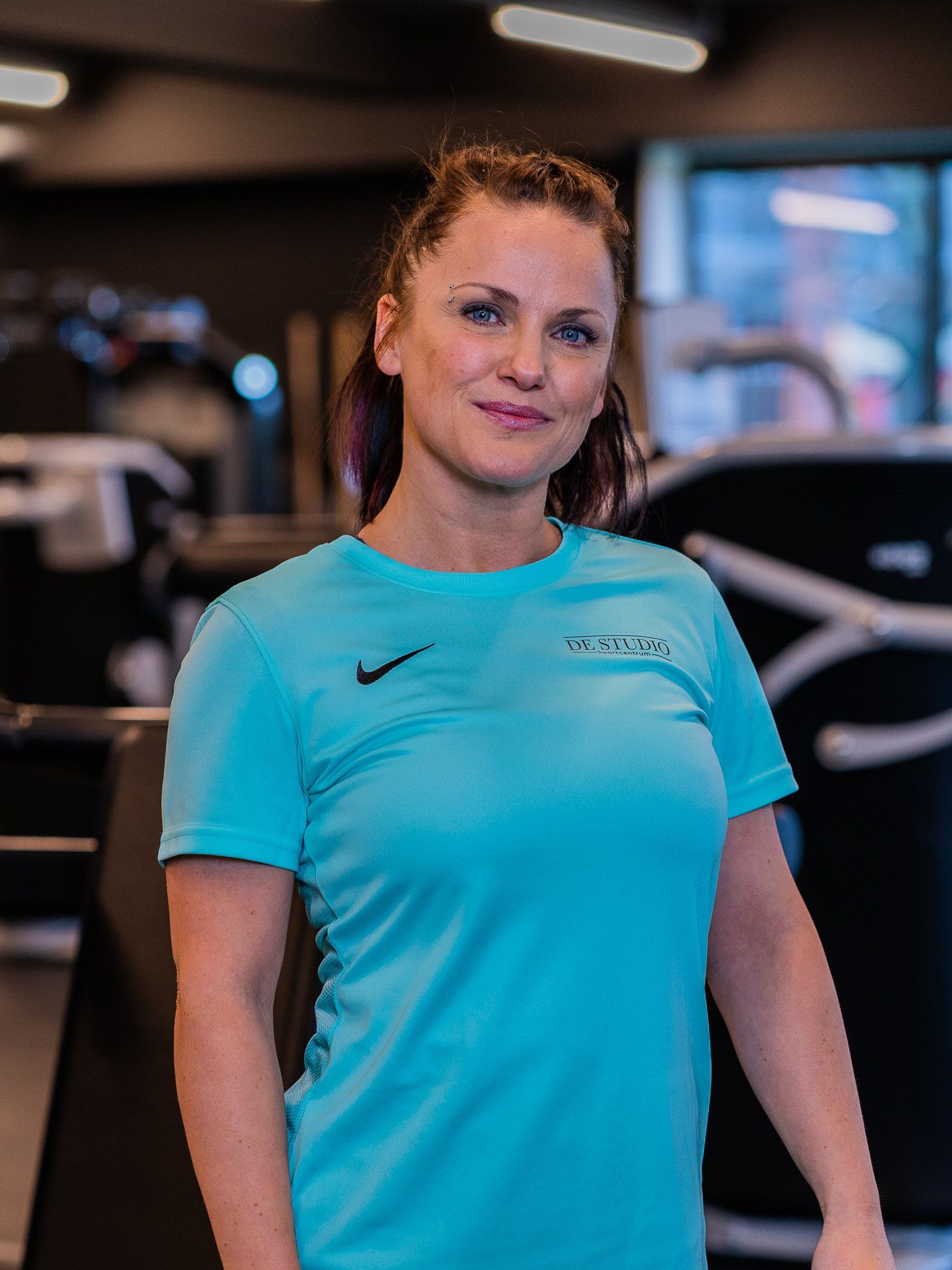 Een vrouw in een blauw Nike-shirt staat in een sportschool.